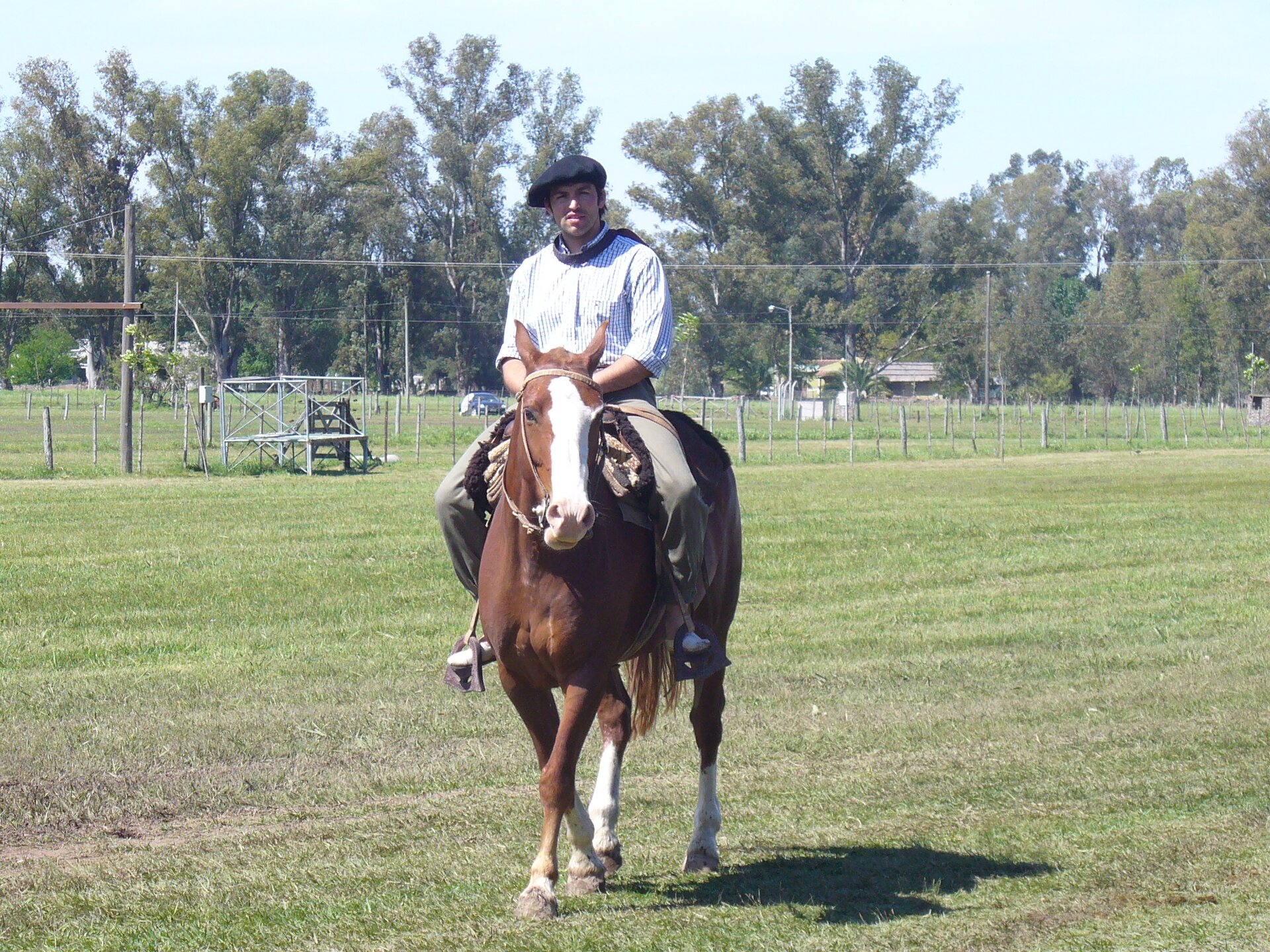 Na zdjęciu mężczyzna siedzi na koniu. Ma na sobie białą koszulę i czarny beret. Wokół płaski teren porośnięty krótką roślinnością trawiastą, w tle las.