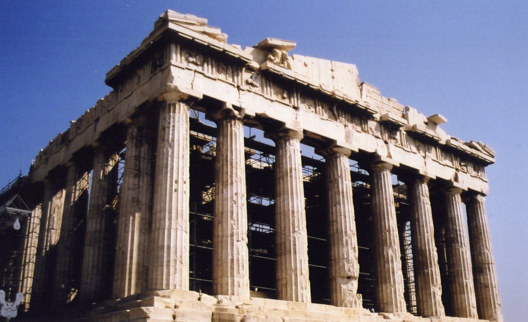 Zdjęcie przedstawia Akropol w Atenach. Budynek wspiera się na szeregu kolumn doryckich. W jego środku widać rusztowania.