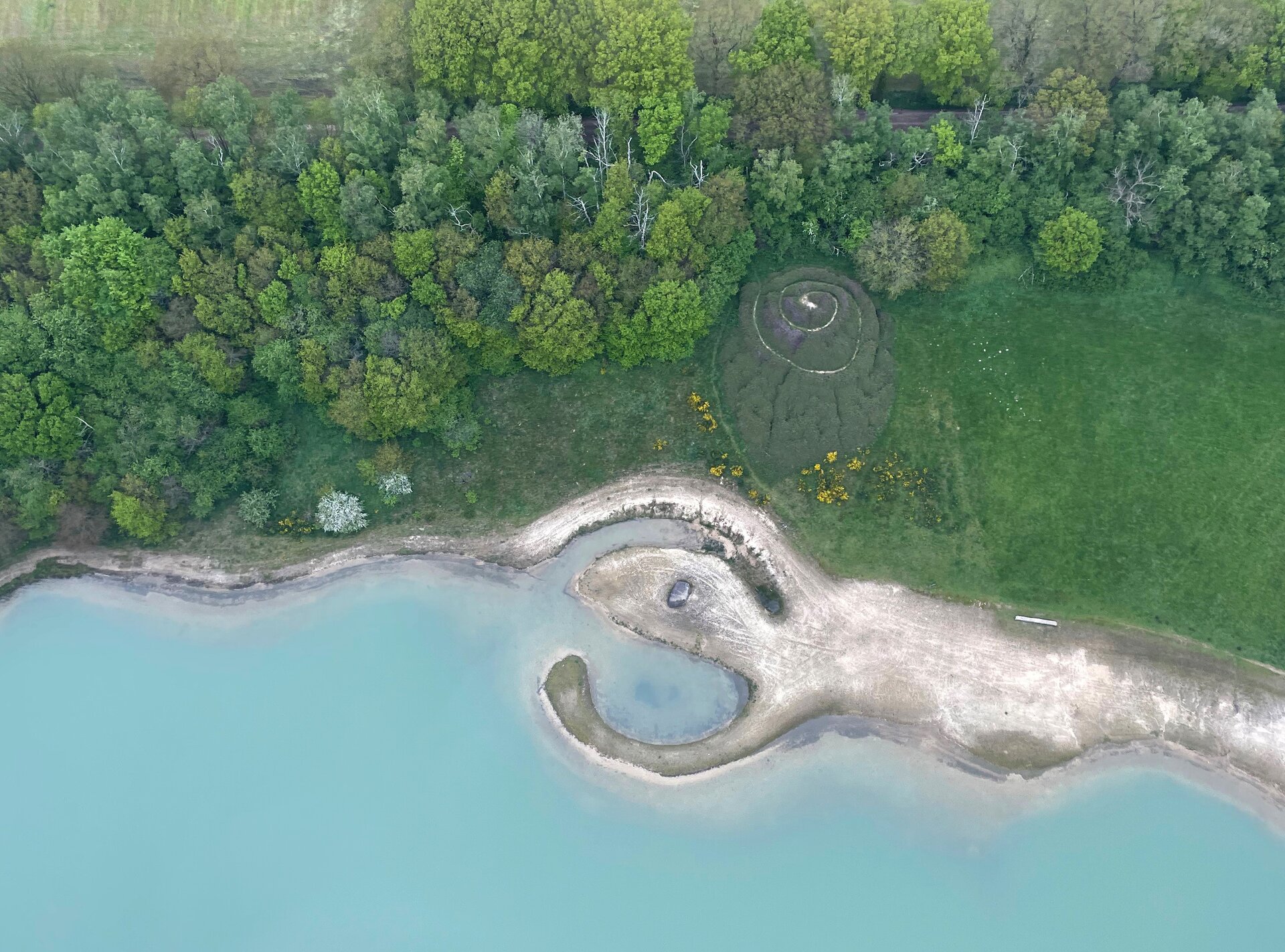 Na zdjęciu wykonanym z nieba dostrzec można w głównej mierze bujny las, u dołu zdjęcia natomiast znajduje się woda, przy której w nieregularnych kształtach prowadzi szara droga. W centrum zlokalizowana jest na wzgórzu dróżka w kształcie spirali prowadząca do najwyższego punktu wzniesienia, a całość porośnięta jest roślinnością.