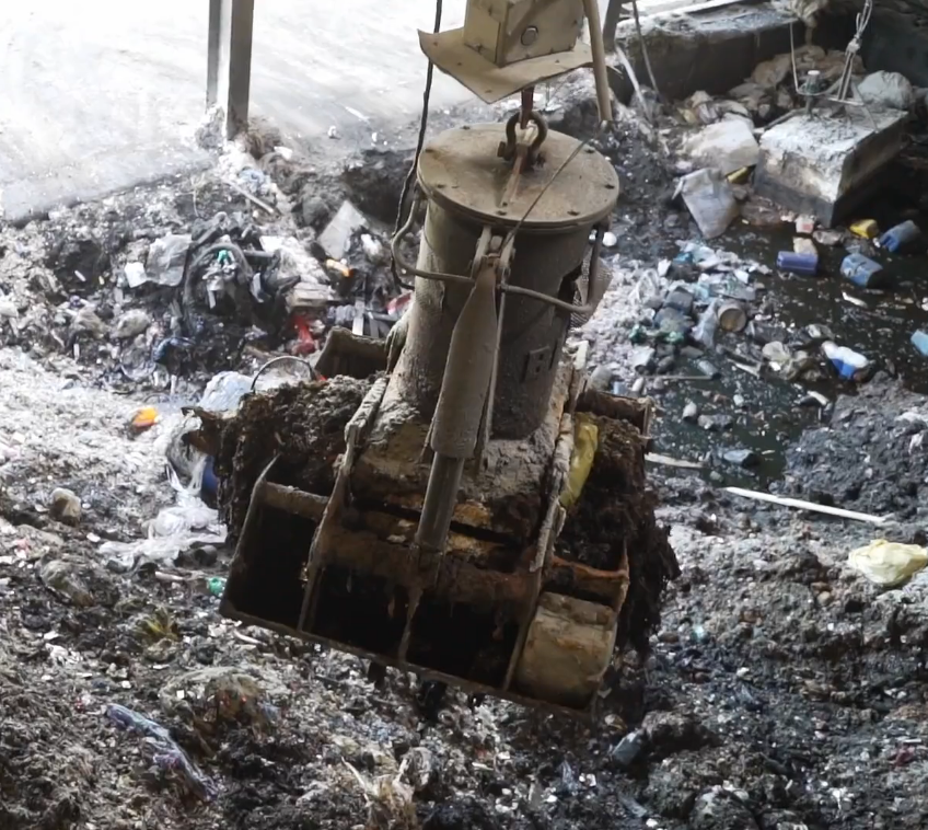 Zdjęcie przedstawia suwnicę załadowczą. To masywne, stalowe urządzenie przenoszące ładunek. Jest zbudowane z otwieranej szeroko na boki łyżki.