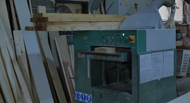 Zdjęcie ukazuje strugarkę. Wystaje z niej kawałek drewna.