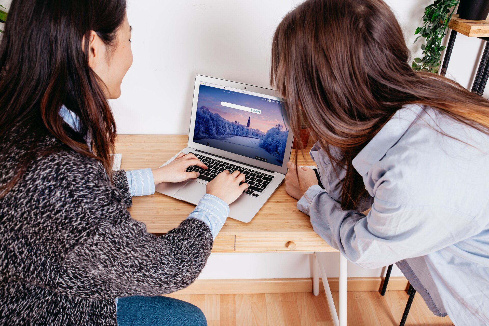 Zdjęcie przedstawia dwie nastolatki, które siedzą przy biurku i przeglądają włączonego laptopa.