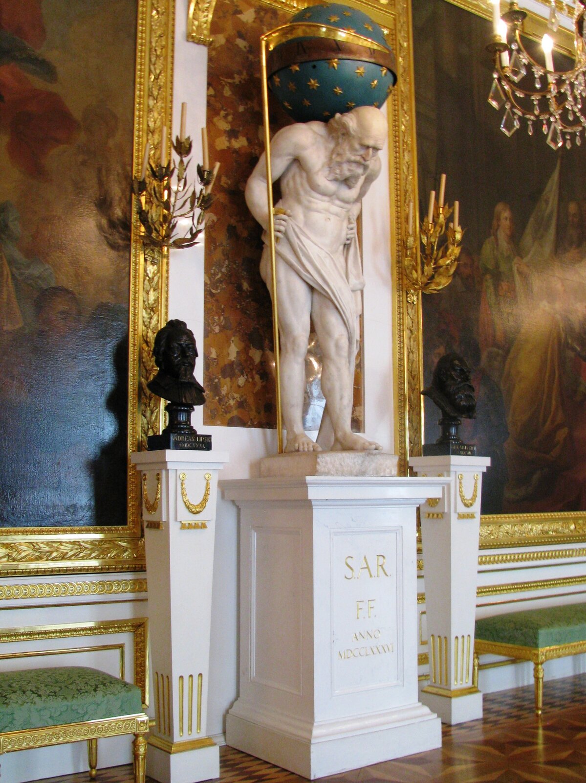 Na zdjęciu znajduje się posąg Chronosa z Sali Rycerskiej na Zamku Królewskim w Warszawie w postaci rzeźby pochylonego starca na cokole. Obnażona jego sylwetka nawiązuje do antyku, zaś głowa odpowiada oświeceniowym wyobrażeniom o mędrcu z długą brodą i bez włosów. Na plecach Chronos trzyma ziemską kulę, która jest mechanizmem zegara regulowanego przez trzymaną przez niego w prawej dłoni postawioną na sztorc kosę.