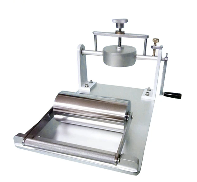 Grafika ukazuje aparat do badania chłonności wody wytworów papierniczych. Składa się ono ze sztywnej podstawy o gładkiej powierzchni i metalowego cylindra oraz urządzenia umożliwiającego docisk cylindra do podstawy.