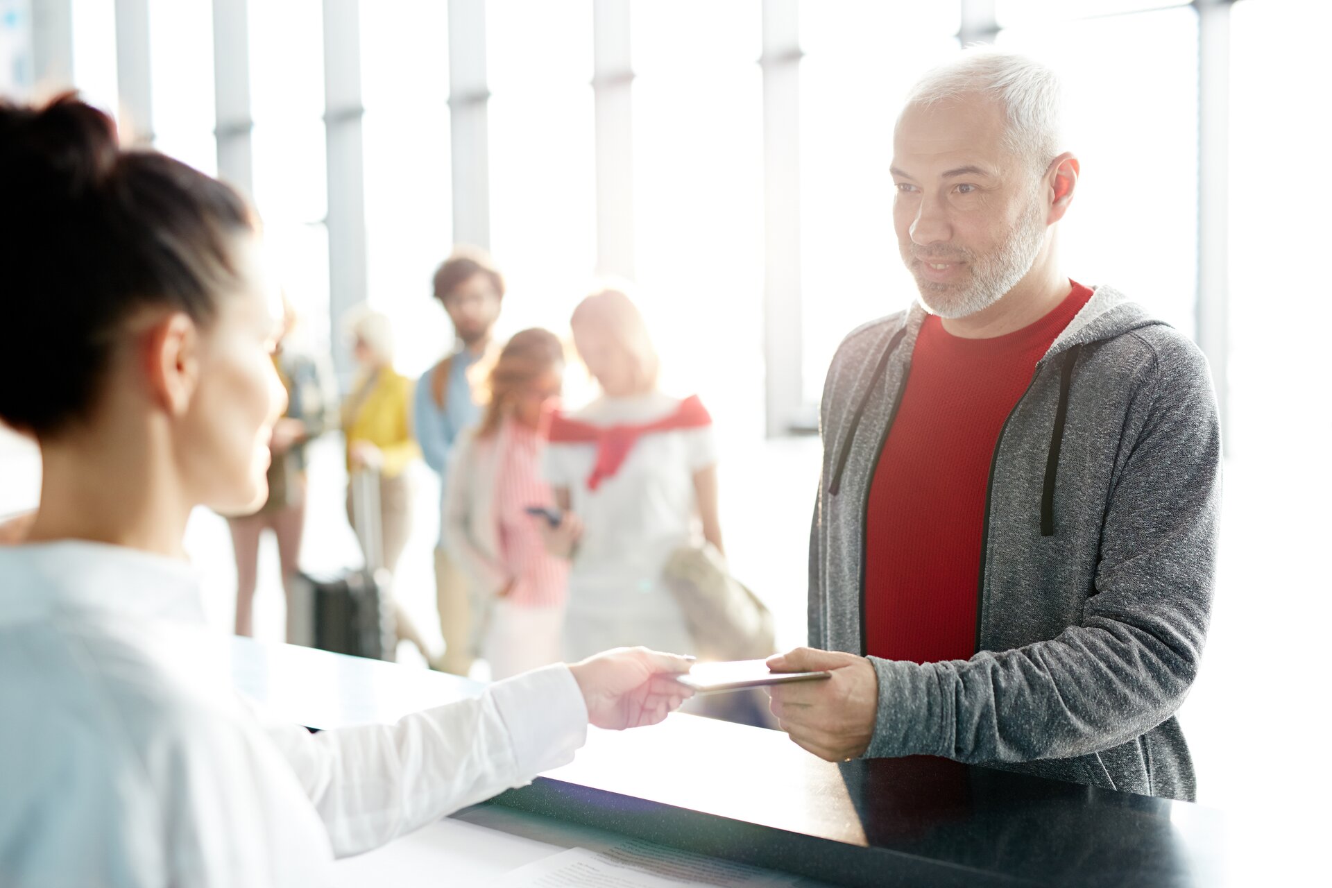 Zdjęcie przedstawia mężczyznę kupującego  bilet w kasie. Za nim ustawiła się długa kolejka. 