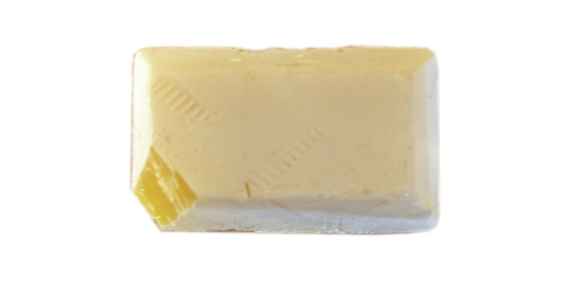 Zdjęcie przedstawia fosfor biały w postaci kremowej kostki z obciętym narożnikiem, przez który widać intensywnie żółte zabarwienie wnętrza kawałka.