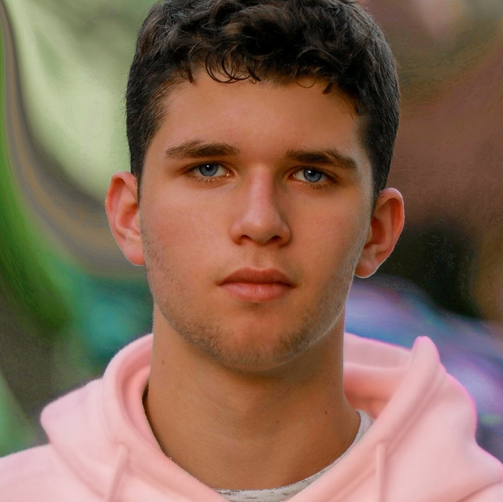 Grafika przedstawia portret nastolatka. Ma ciemne, krótkie włosy i niebieskie oczy. Patrzy w obiektyw.