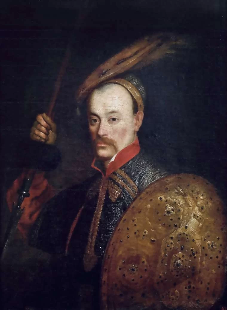 Kliknij, aby powiększyć. Na obrazie przedstawiono portret hetmana polnego litewskiego Wincentego Korwin Gosiewskiego. Na głowie ma czapkę z dużym piórem. W prawej ręce trzyma włócznię, a w lewej tarczę.