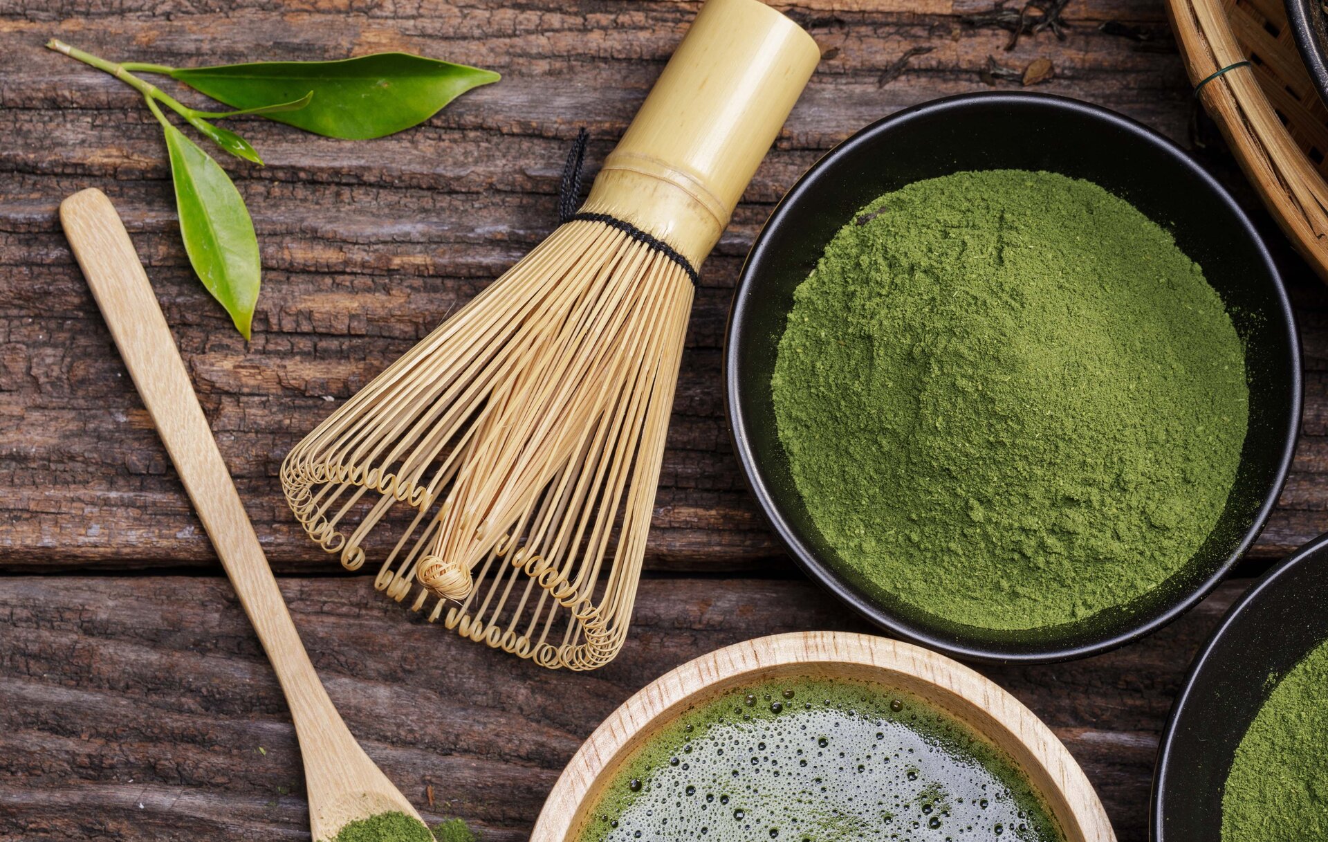 Zdjęcie przedstawia trzepaczkę wiklinową do zielonej herbaty w proszku oraz miseczki z zielonym proszkiem i gotowym naparem.