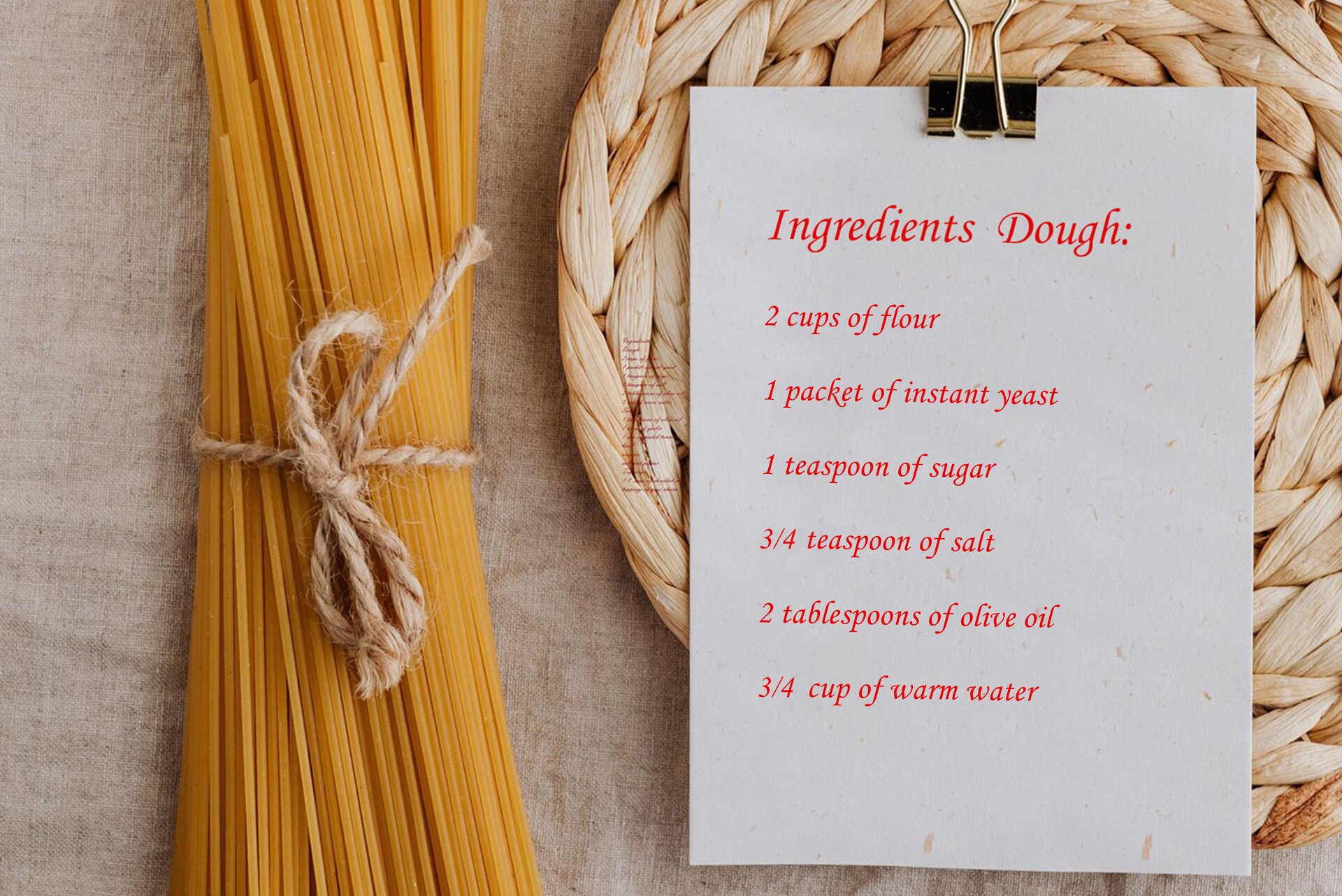 Zdjęcie przedstawia leżące na lnianej, szarej tkaninie: po lewej – makaron spaghetti związany szarym sznurkiem, a po prawej – kartkę przypiętą dużym spinaczem, leżącą na plecionej podkładce. Na kartce widoczny przepis na ciasto w języku angielskim: Ingredients Dough: 2 cups of flour, 1 packet of instant yeast, 1 teaspoon of sugar, 3/4  teaspoon of salt, 2 tablespoons of olive oil, 3/4 cup of warm water.