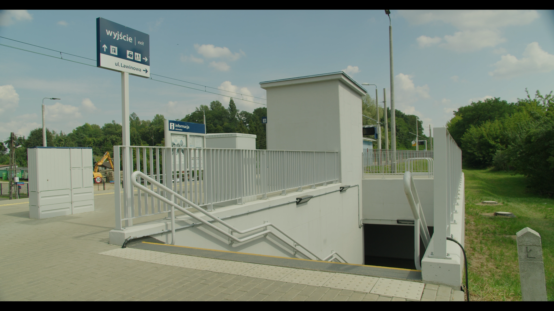 Ilustracja przedstawia przejście pod torami. Widoczny jest peron kolejowy oraz schody prowadzące w dół, ogrodzone barierkami.