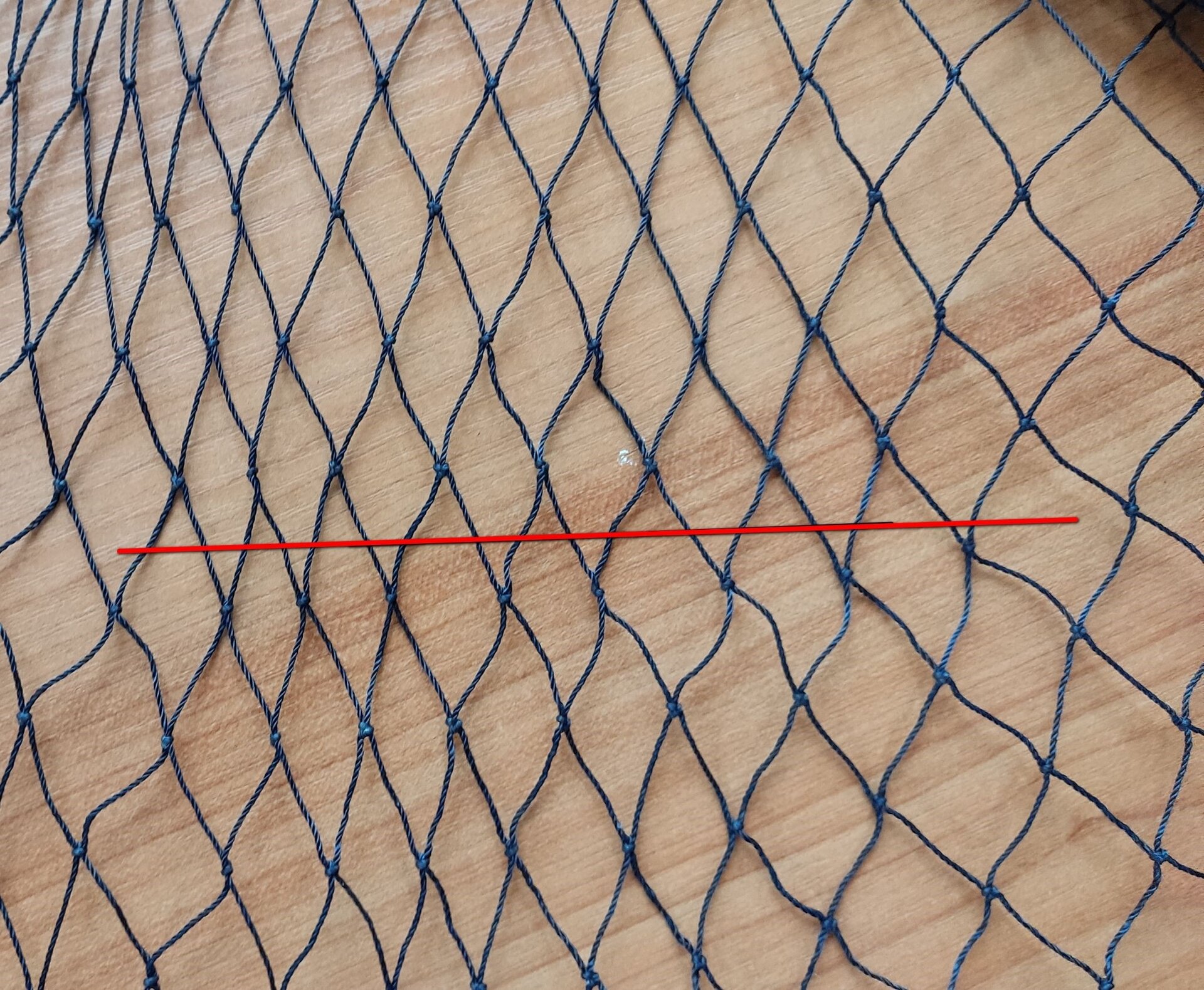Zdjęcie przedstawia cięcie proste sieci rybackiej. Jest to cięcie przyległych boków oczek równolegle do długości lub szerokości sieci