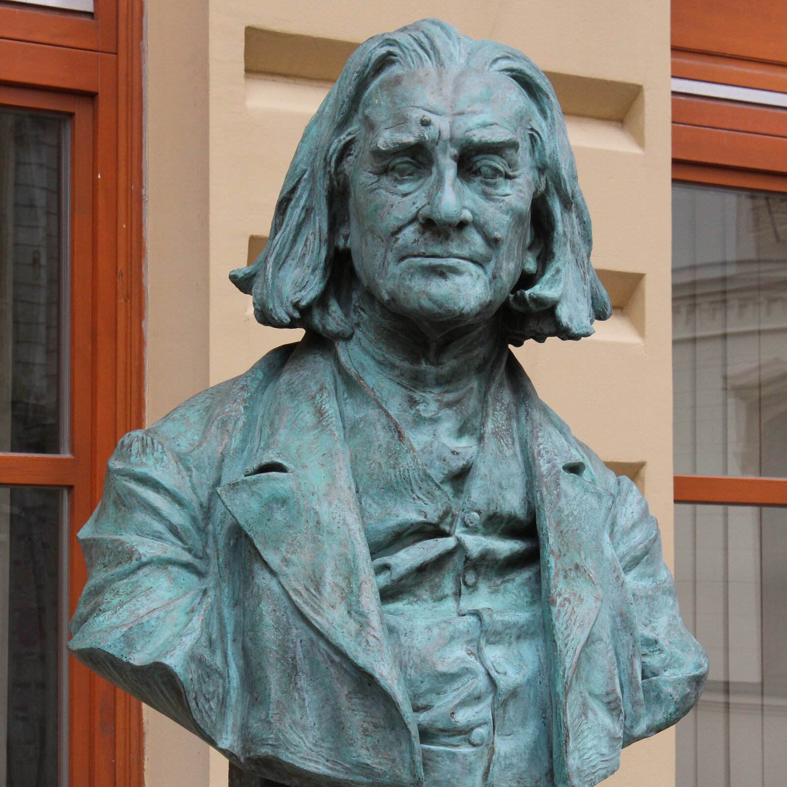 Na zdjęciu przedstawiono popiersie Ferenca Liszta. Popiersie jest pokryte zielonym nalotem. Mężczyzna jest lekko zgarbiony, ma głowę wysuniętą do przodu. Ma duży nos, pieprzyki na twarzy, zmarszczki na czole i pod oczami. Jego włosy są gęste, długości przed ramiona. Jest ubrany w płaszcz, a pod spodem w kamizelkę.