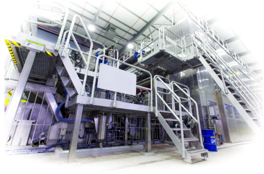 Na grafice przedstawiona jest prasa klejarska od boku. Jest to duża maszyna z wieloma elementami. Z boku znajdują się schody umożliwiające wejście na górę maszyny.