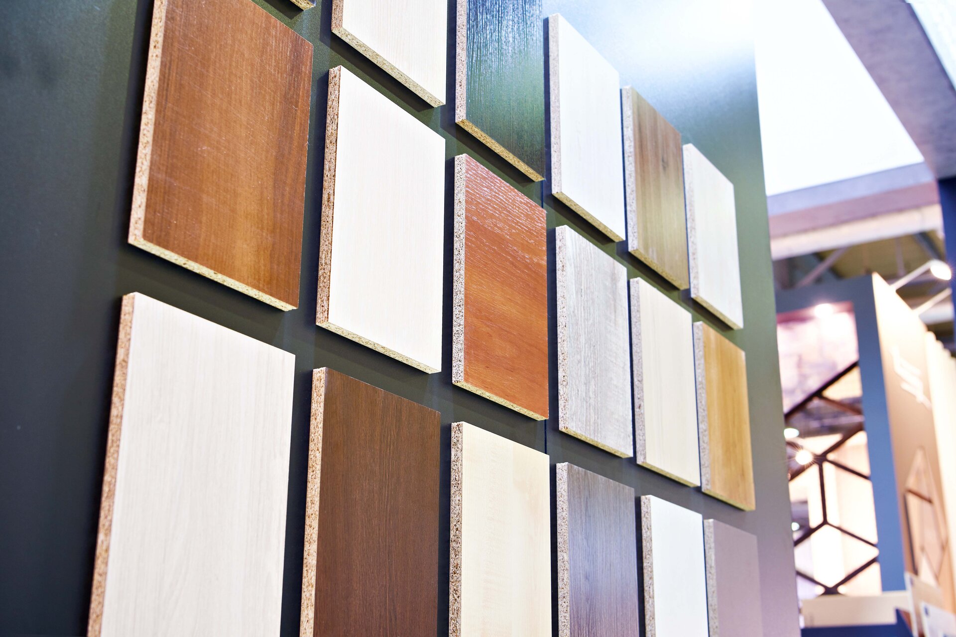 Zdjęcie przedstawia kilkanaście fornirowanych płyt HDF niedużej wielkości, zawieszonych na ścianie, o różnych odcieniach.