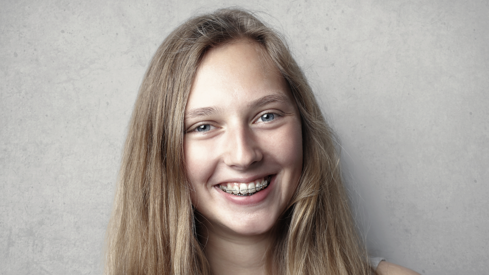 Kobieta na zdjęciu ma szeroki uśmiech i patrzy bezpośrednio w obiektyw. Kobieta wygląda na szczęśliwą.