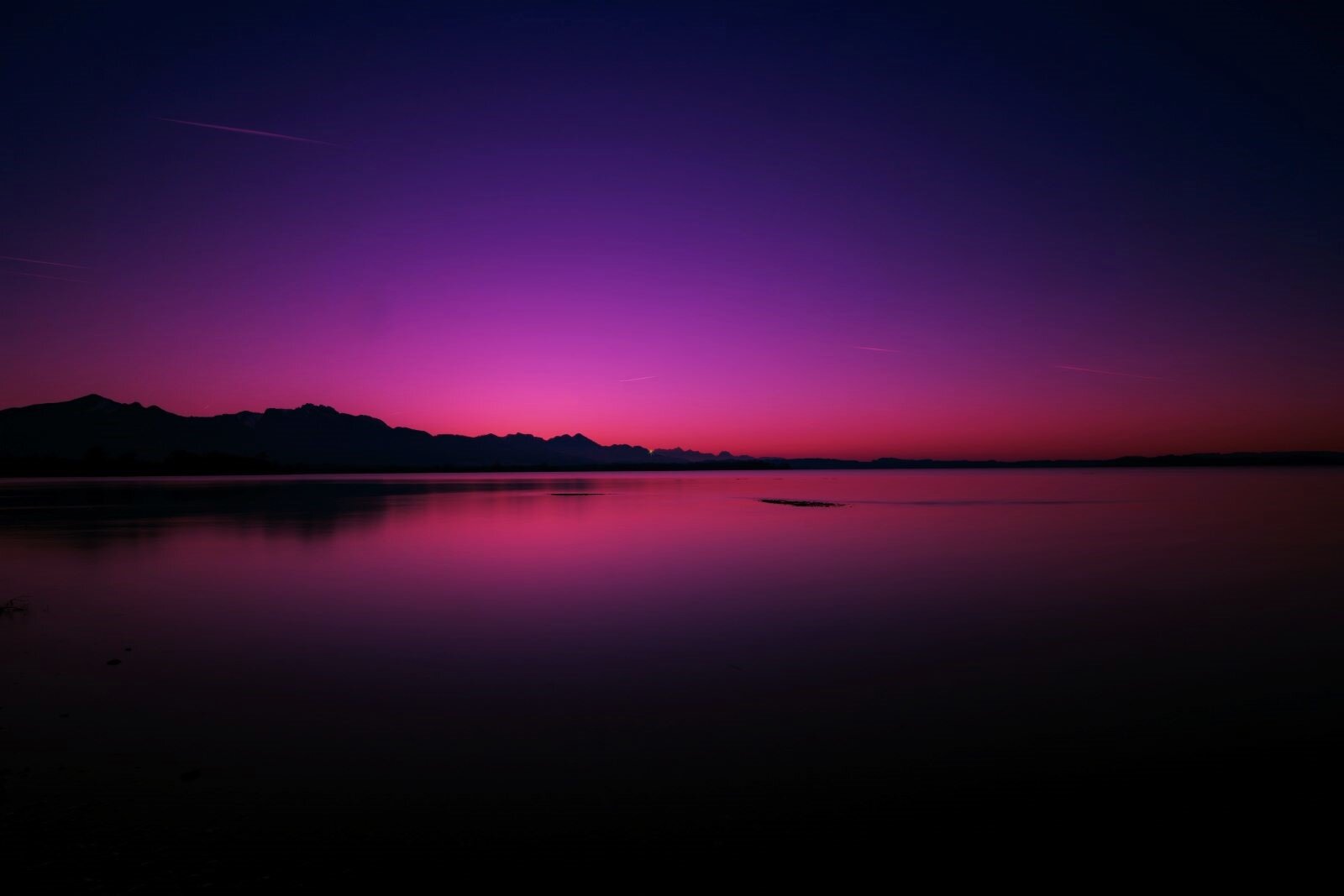 Zdjęcie przedstawia nastrojową fotografię - zatokę, z niewielkimi wzniesieniami na horyzoncie, które odbijają się w wodzie. Woda i niebo są jak lustro, wszystko w zimnych barwach, lekko ciepłych przy linii horyzontu.