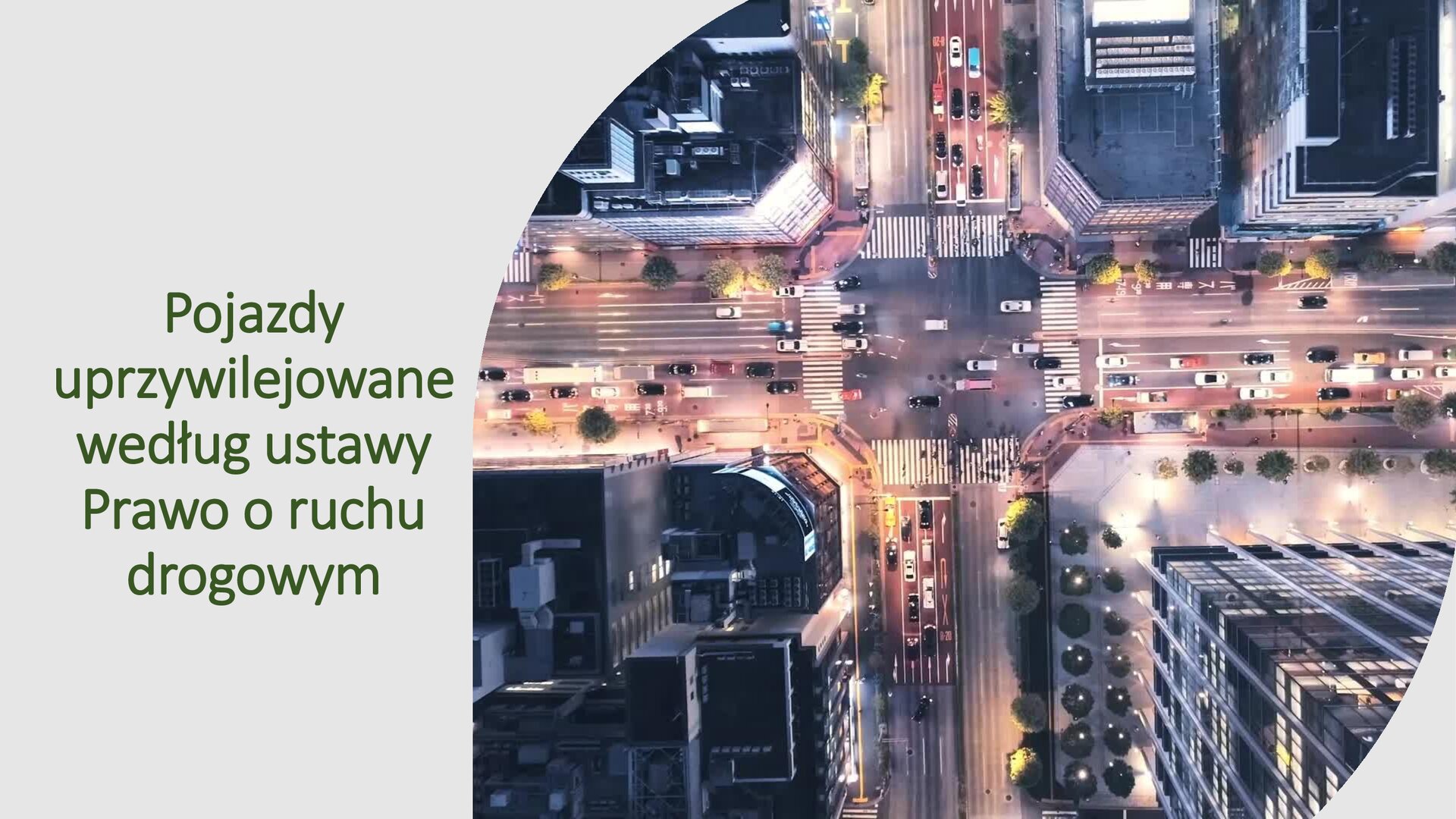 Szary slajd. Z lewej strony tekst: „Pojazdy uprzywilejowane według ustawy Prawo o ruchu drogowych”. Z prawej strony zdjęcie z lotu ptaka, ukazujące dachy wieżowców, a między nimi oświetlone ulice, po których jeżdżą samochody.