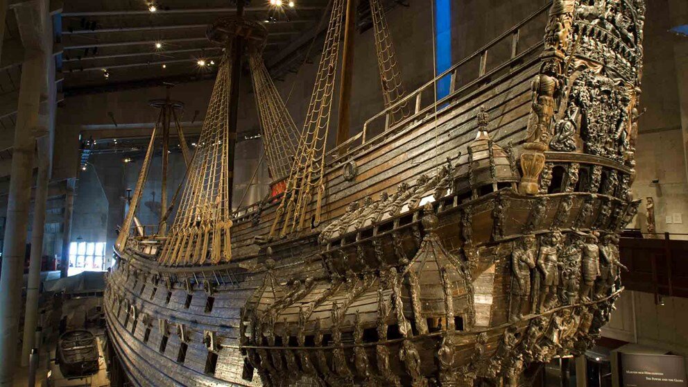 Zdjęcie przedstawia siedemnastowieczny galeon wojenny Vasa, który był budowany według wskazówek Gustawa Adolfa. Jest to statek zbudowany z drewna z potężną burtą. Pokłady są na dwóch poziomach, niższy pokład po prawej stronie statku i wyższy po lewej. Z przodu statku wyrzeźbiono dekoracyjne wykończenie i umieszczono bogato zdobione balustrady. Są tam liczne płaskorzeźby przedstawiające między innymi ludzi. Statek ten posiada trzy maszty i masywny dziób.