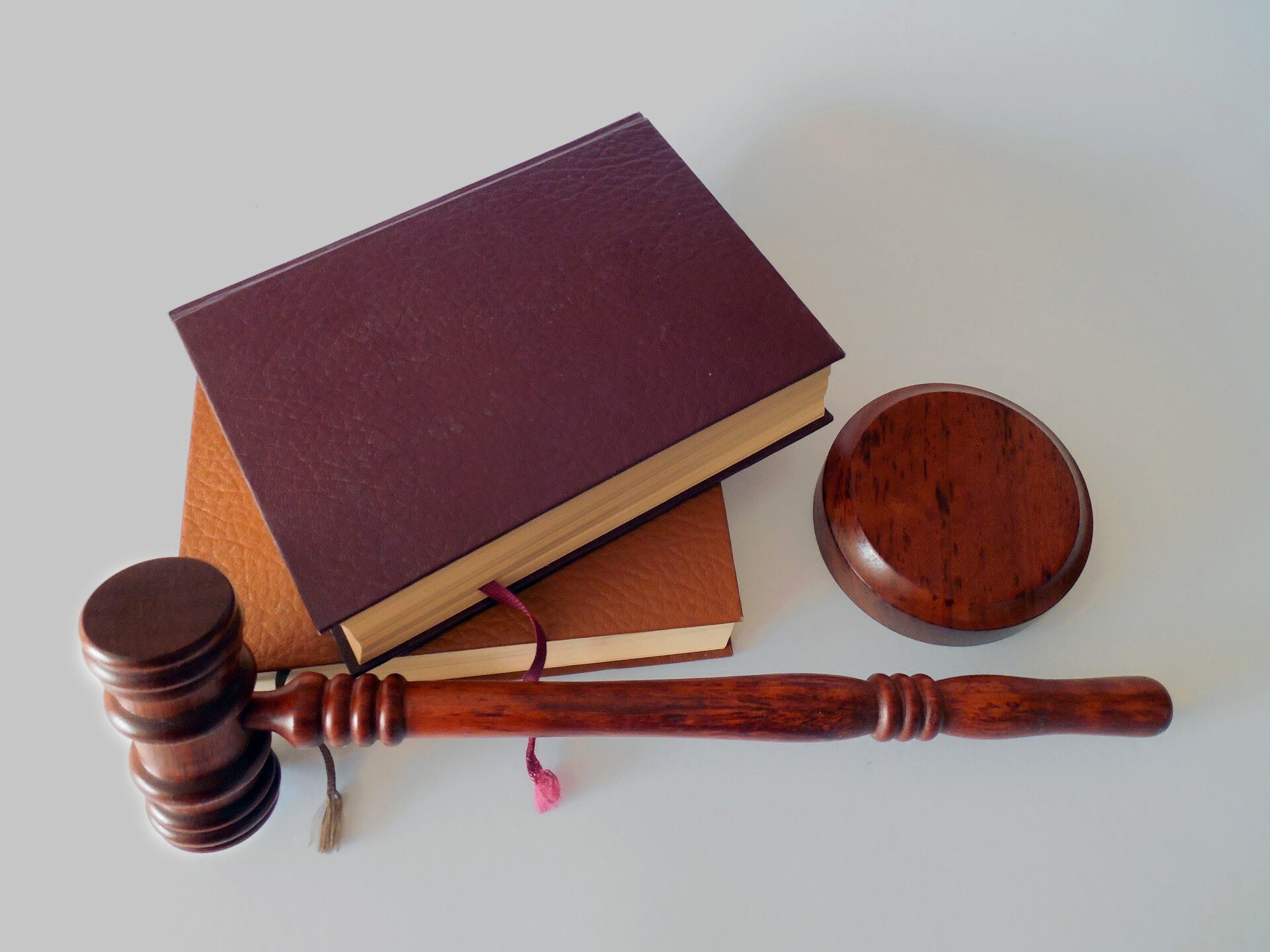 Zdjęcie przedstawia młotek sędziowski i podstawkę. Obok nich leżą dwie książki w skórzanych oprawach.