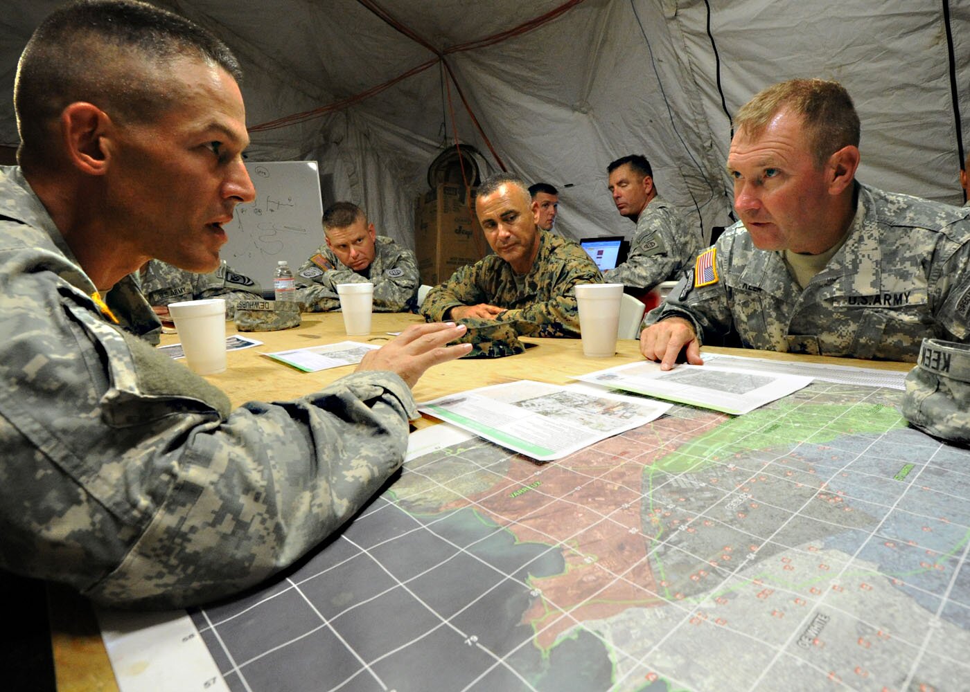 Fotografia przedstawiająca amerykańskich żołnierzy siedzących w namiocie przy stole i żywo dyskutujących nad mapą