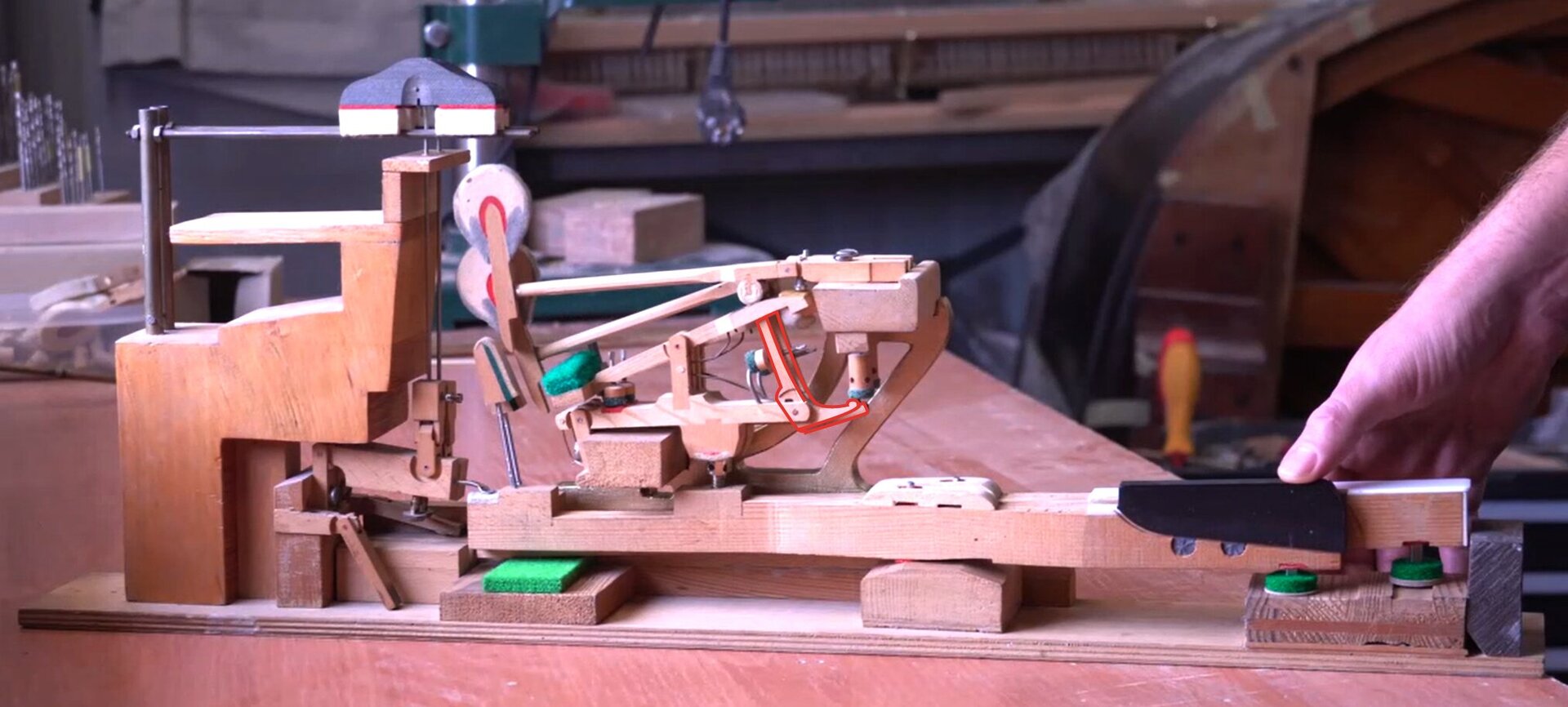 Zdjęcie przedstawia podzespół mechanizmu pianinowego lub fortepianowego jakim jest popychacz. Element został zaznaczony czerwoną obwódką, a dodatkowo pozostałe elementy są w odcieniach szarości dla lepszego uwidocznienia.