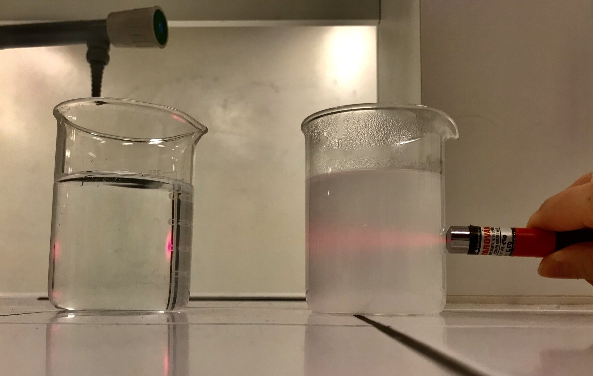 Ilustracja demonstruje, jak światło przechodząc przez roztwór koloidalny, ulega rozproszeniu na cząsteczkach, czego skutkiem jest rozszerzenie wiązki i powstanie tzw. stożka Tyndalla. Na zdjęciu widoczna jest ciecz w zlewce widziana z boku. Przez szklaną ściankę zlewki do cieczy wpada wiązka lasera czerwonego. W rezultacie wewnątrz cieczy widoczny jest jasny czerwony klin. Światło ulega stopniowemu rozproszeniu wewnątrz cieczy. 