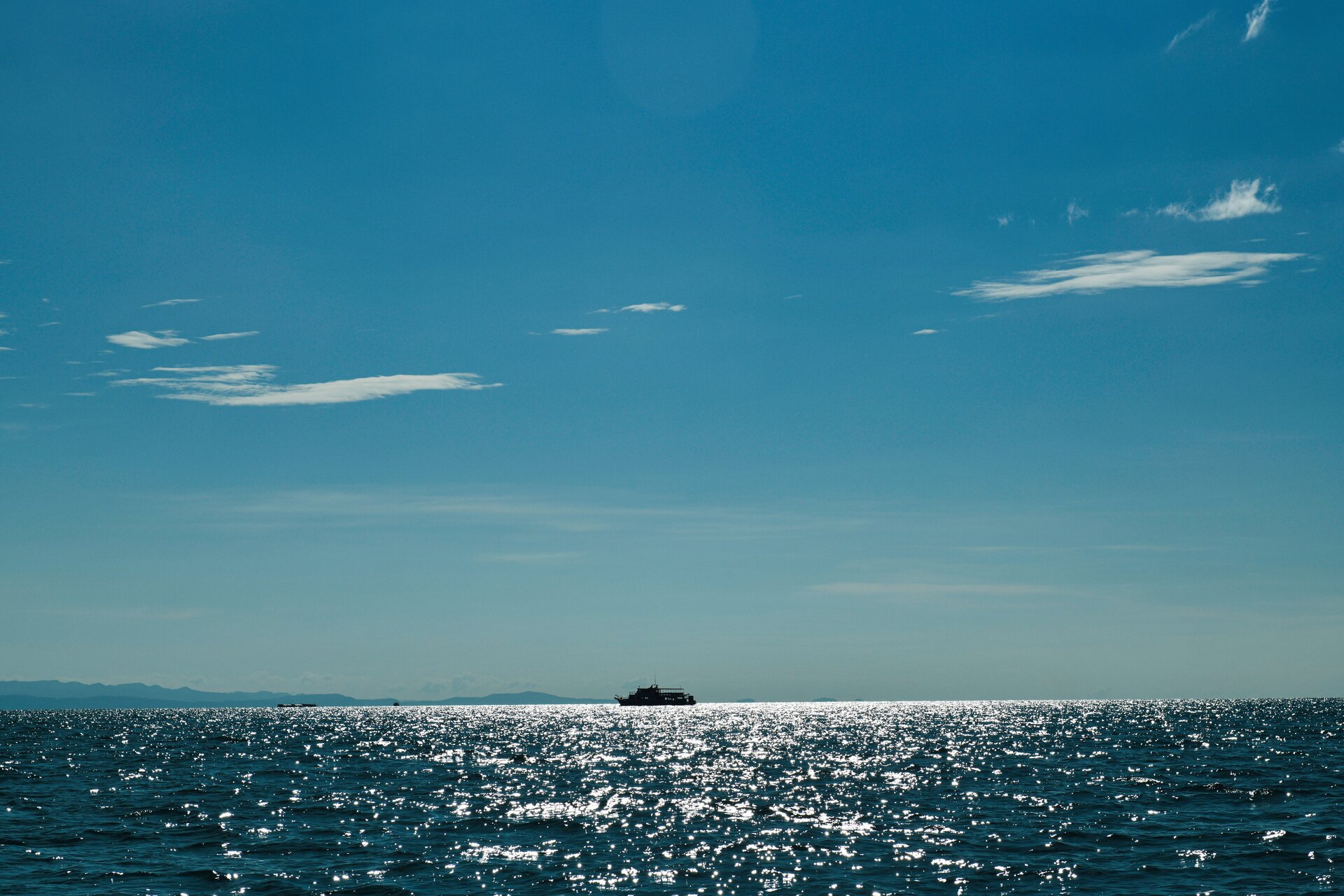 Zdjęcie przedstawia gładką powierzchnię morza w bezwietrzny dzień. Daleko, na horyzoncie znajduje się statek. Niebo jest niemal bezchmurne.