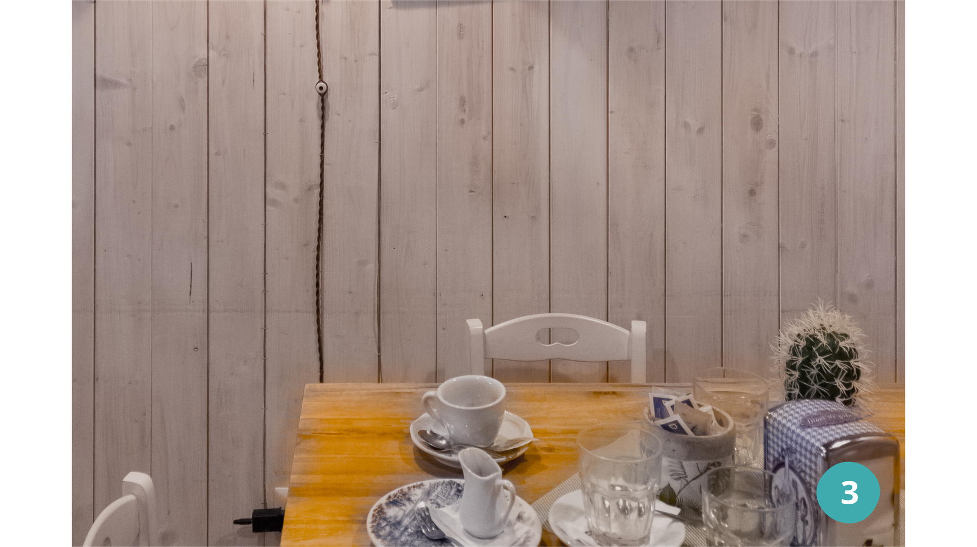 Zdjęcie przedstawia stół, na którym stoją naczynia, pojemnik na serwetki, kaktus. Za stołem stoją krzesła.