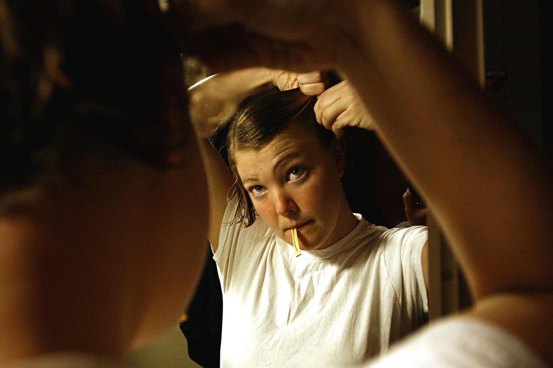 Zdjęcie przedstawia dziewczynę stojącą przed lustrem. Układa sobie fryzurę, wpinając w nią spinki. Jedną ze spinek trzyma w ustach, jedną ręką przytrzymuje sobie włosy, a drugą wpina ozdobę. Zadanie alternatywne wyświetla się w trybie dostępności.