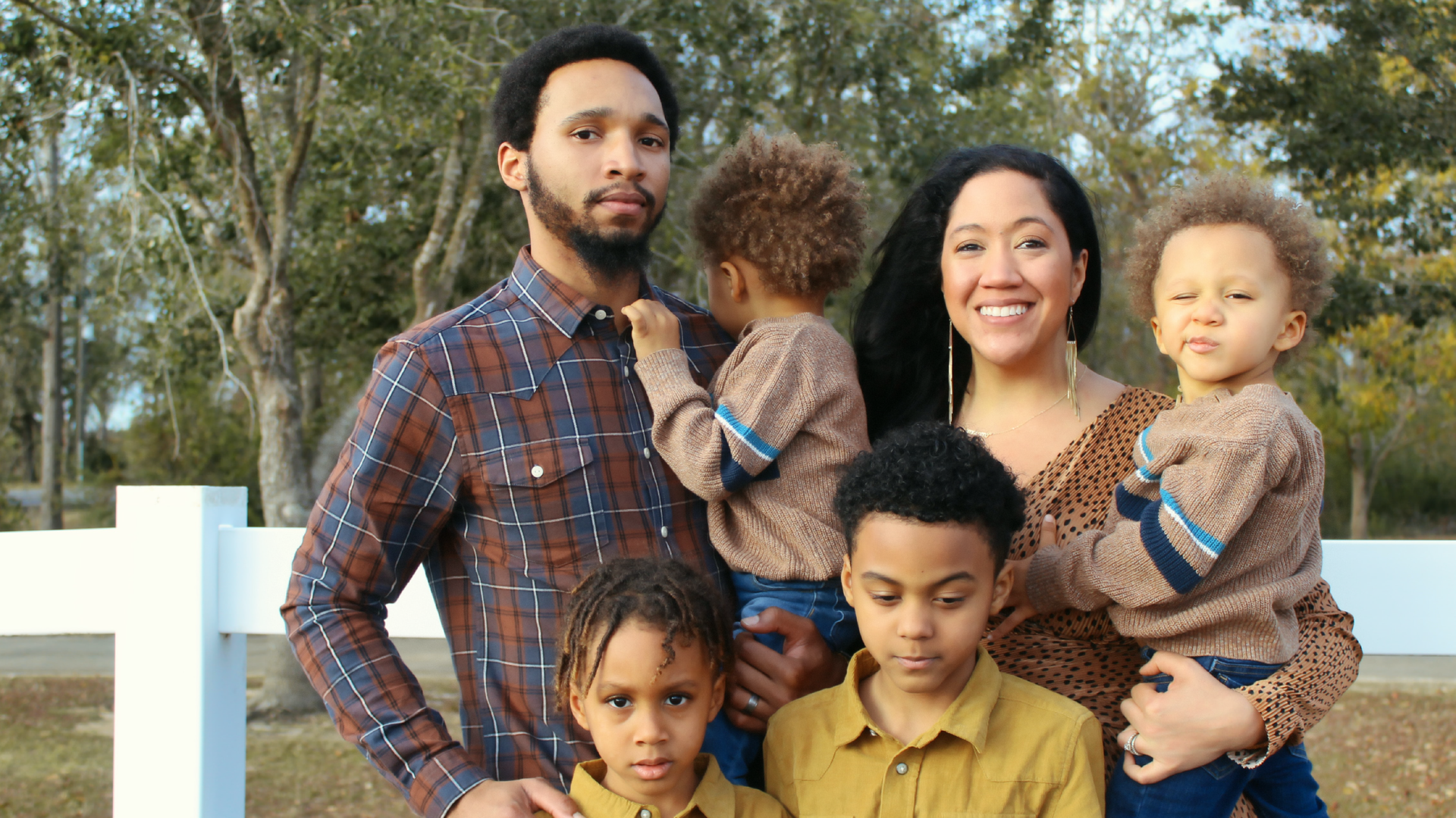 Zdjęcie przedstawia rodzinę na tle lasu. W górnym rzędzie od lewej stoi ojciec i trzyma małe dziecko na ręku. Obok ojca stoi uśmiechnięta matka z małym dzieckiem na ręku. W dolnym rzędzie stoi dwóch chłopców, po lewej niższy i młodszy, po prawej starszy i wyższy.