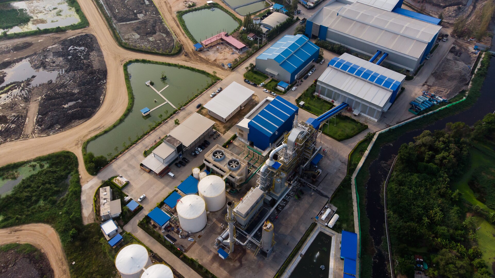 Ilustracja przedstawia kompleks budynków spalarni. Widoczne są hale, magazyny, ogromne wentylatory i walcowate silosy.