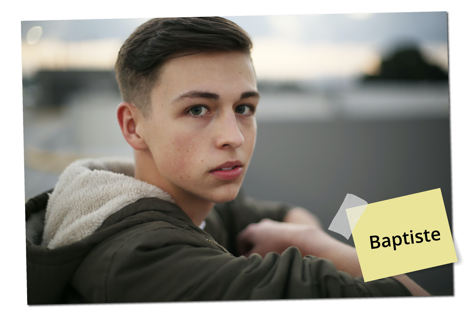 Na zdjęciu widoczny jest chłopak o brązowych włosach, ubrany w zieloną kurtkę z kapturem. Na zdjęciu znajduje się podpis: Baptiste.