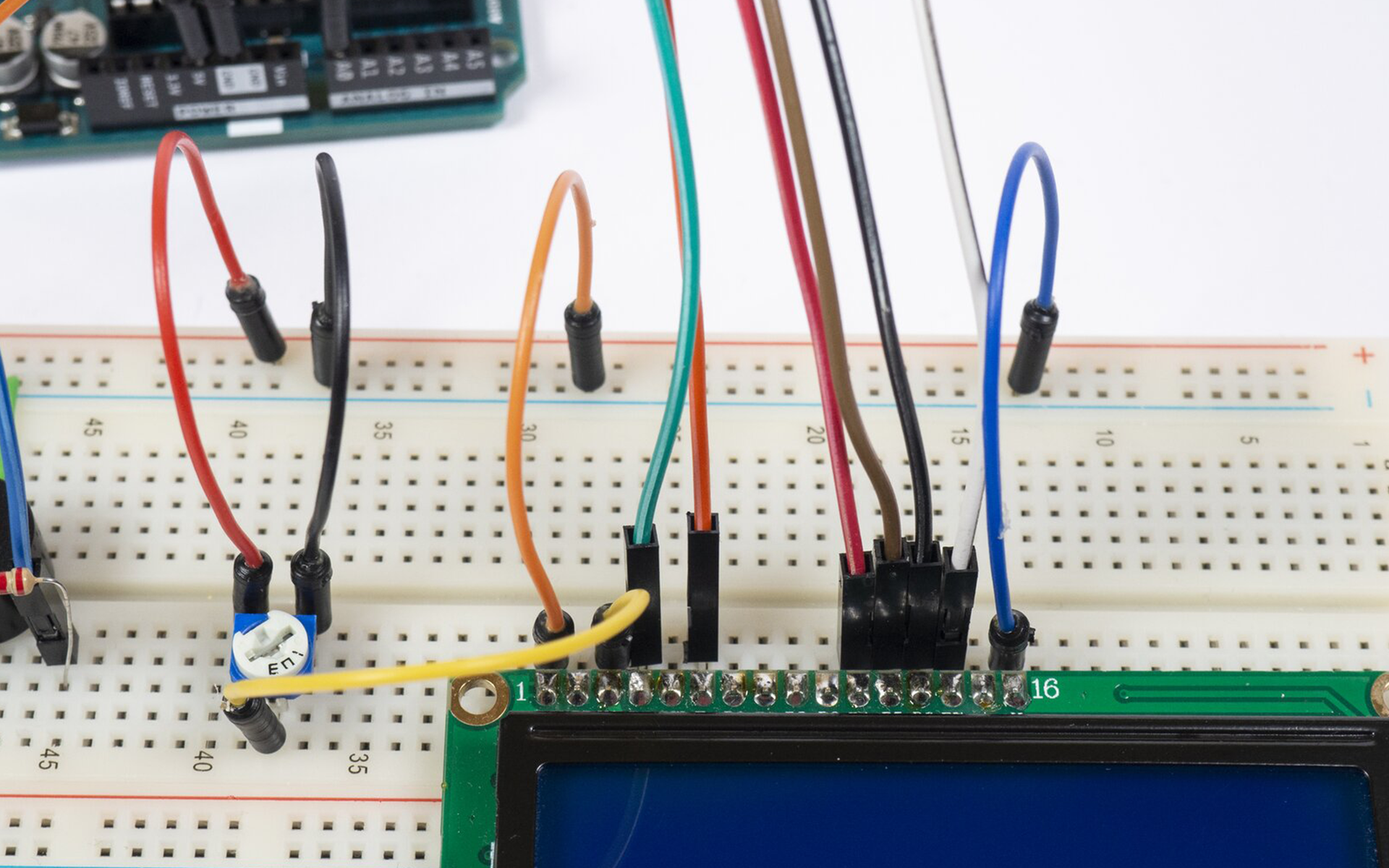 Zdjęcie przedstawia połączenia pomiędzy arduino uno, a płytką stykową. Na płytce znajduje się termometr (względem wycięcia w obudowie) podłączony jest prawą nóżką do uziemienia, lewą do +5V a środkową do pinu A0 arduino. Pin 5V podłączony jest do +5V płytki, a GND podłączone jest do uziemienia. Uziemienie górnej szyny jak i dolnej na płytce stykowej jest połączone. Podłączona jest także LED, jedną nóżką do uziemienia, drugą zaś poprzez rezystor do pinu 7 arduino. Po środku płytki zamontowany jest brzęczyk, który poprzez rezystor łączy się z pinem 6 arduino, a drugą nóżką do uziemienia. Po prawej stronie płytki stykowej podłączono ekran LCD, do którego podłączono kable prowadzące do arduino. Pomiędzy ekranem a brzęczykiem zamontowano potencjometr, do jego nóżek podłączono kable, środkowy do 3 pinu ekranu, lewa nóżka do +5V natomiast prawy do uziemienia. Ostatni i pierwszy pin ekranu podłączono do uziemienia płytki.