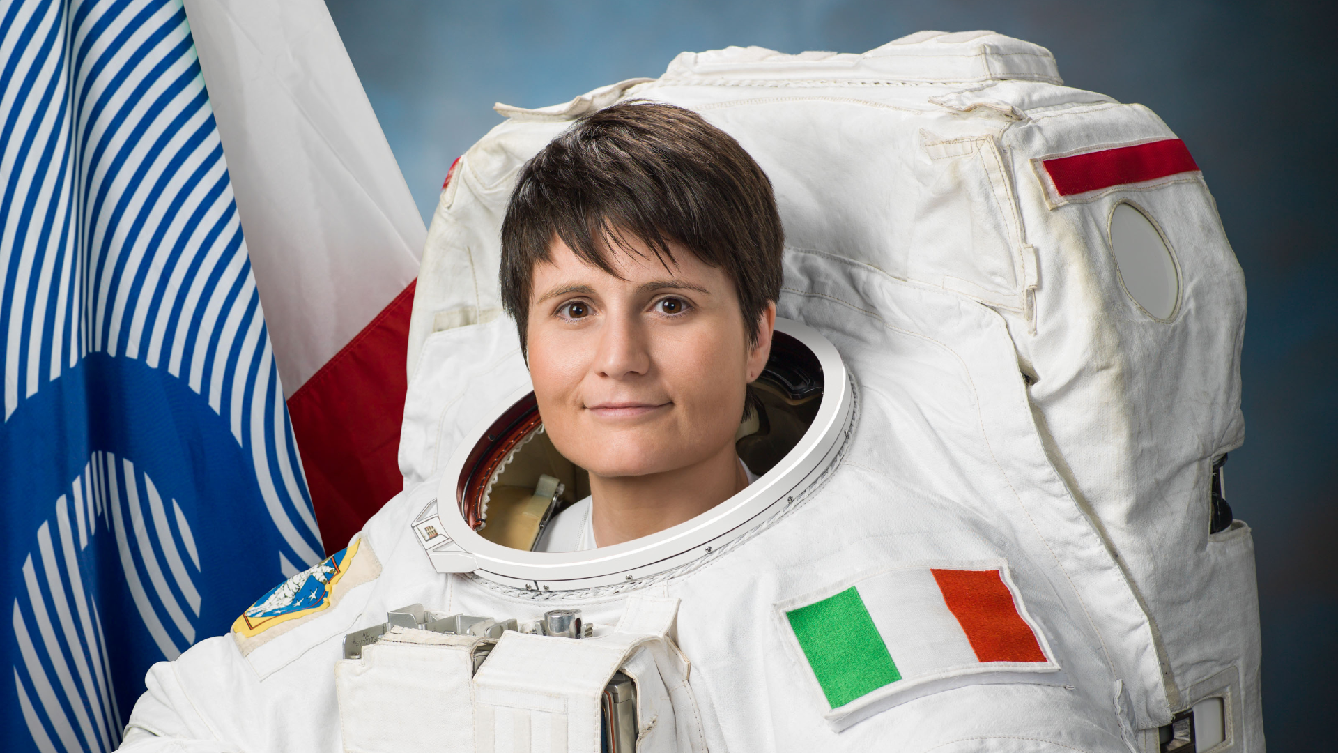 Zdjęcie przedstawia włoską astronautkę. Ubrana jest w kombinezon dla astronautów. Na ramieniu znajduje się włoska flaga. Nazywa się Samantha Cristoforetti.
