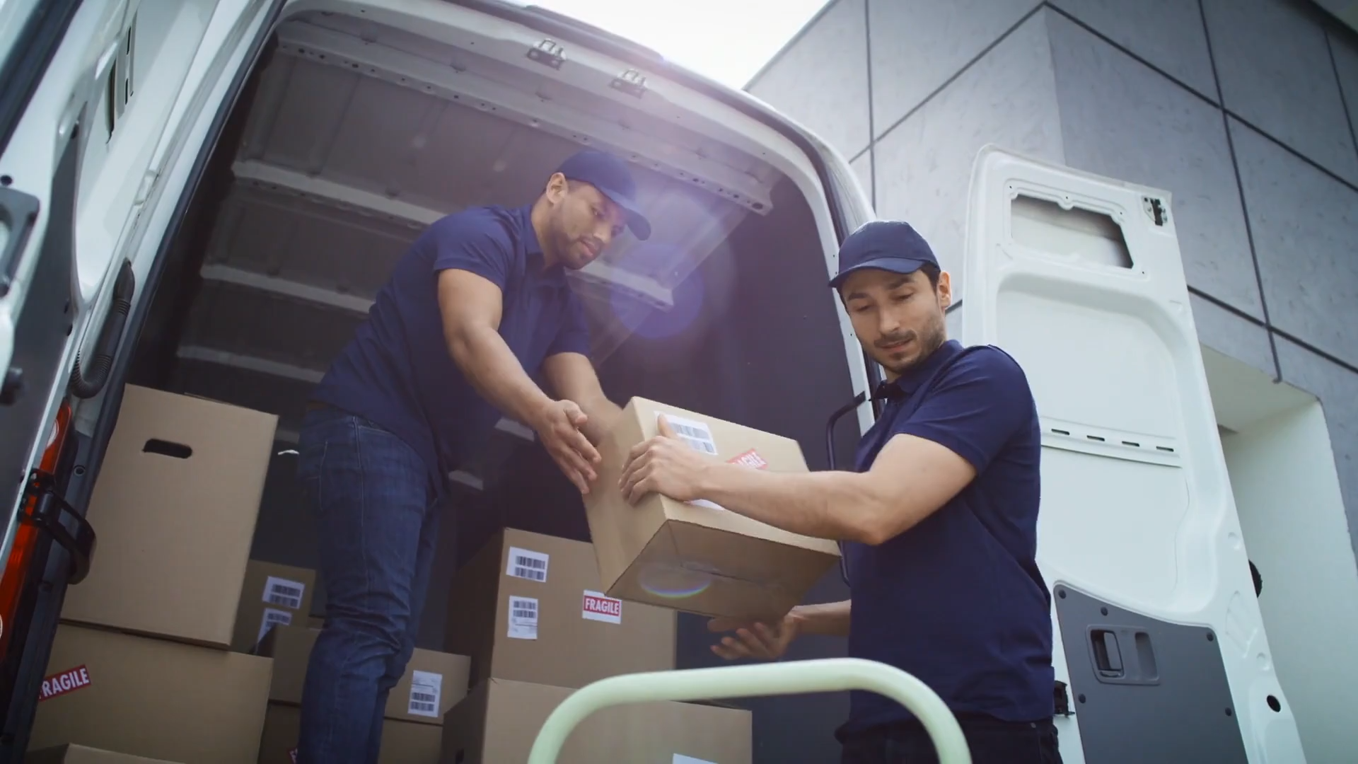 Zdjęcie przedstawia dwóch mężczyzn wyładowujących ładunki drobnicowe z samochodu dostawczego.