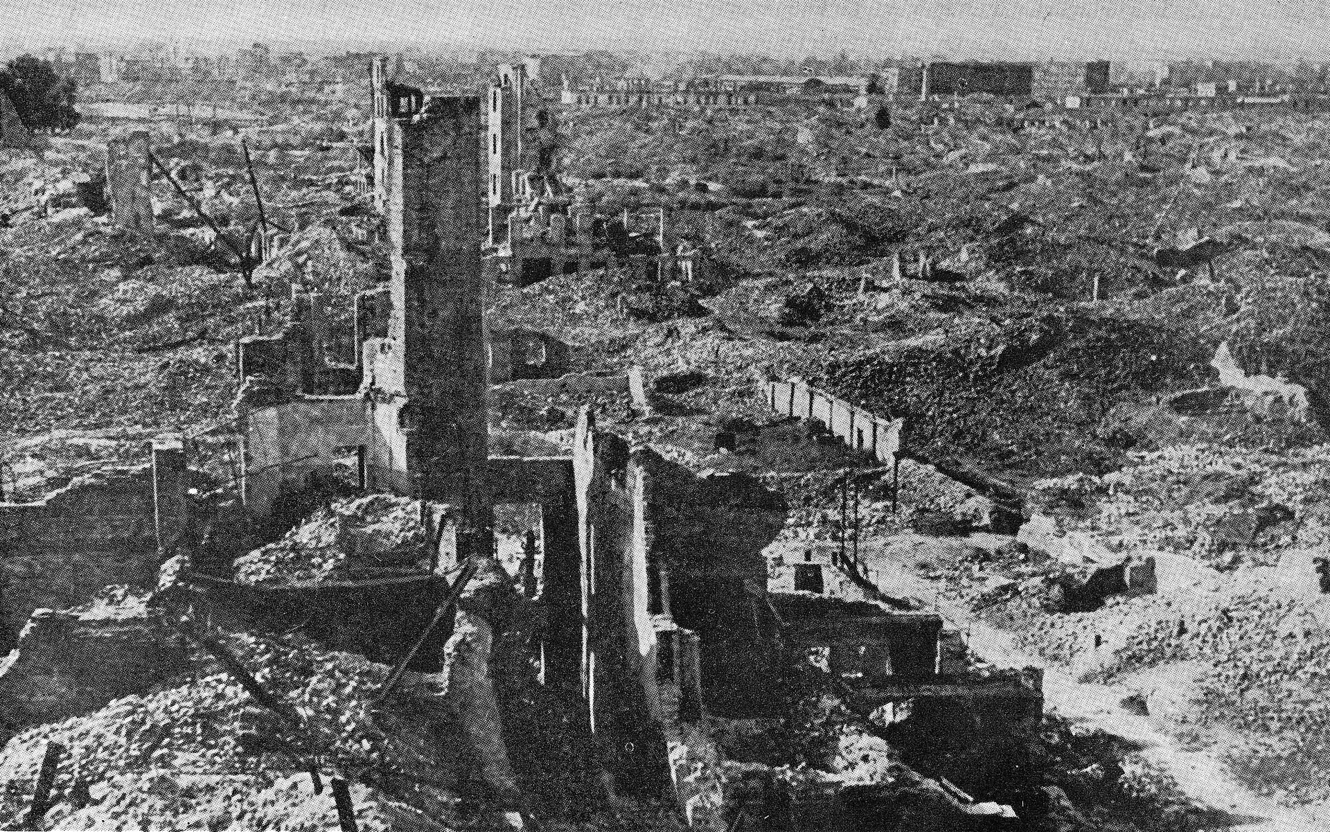 Czarno‑biała fotografia przedstawia ruiny warszawskiego getta. Gdzieniegdzie znajdują się pozostałości po zbombardowanych budynkach: fragmenty ścian, otwory, w których kiedyś były okna czy drzwi. Dominującym elementem na zdjęciu jest leżący gruz.