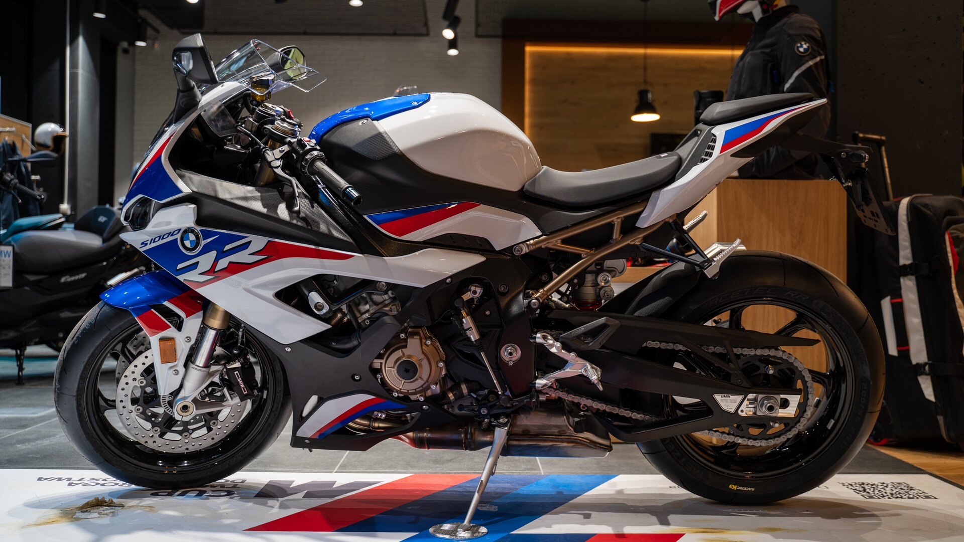 Zdjęcie przedstawia masywny motocykl. Ma biało‑niebiesko‑czerwoną obudowę, głównie w przedniej części motocykla. Pojazd ma bardzo krótka przednią szybę. 