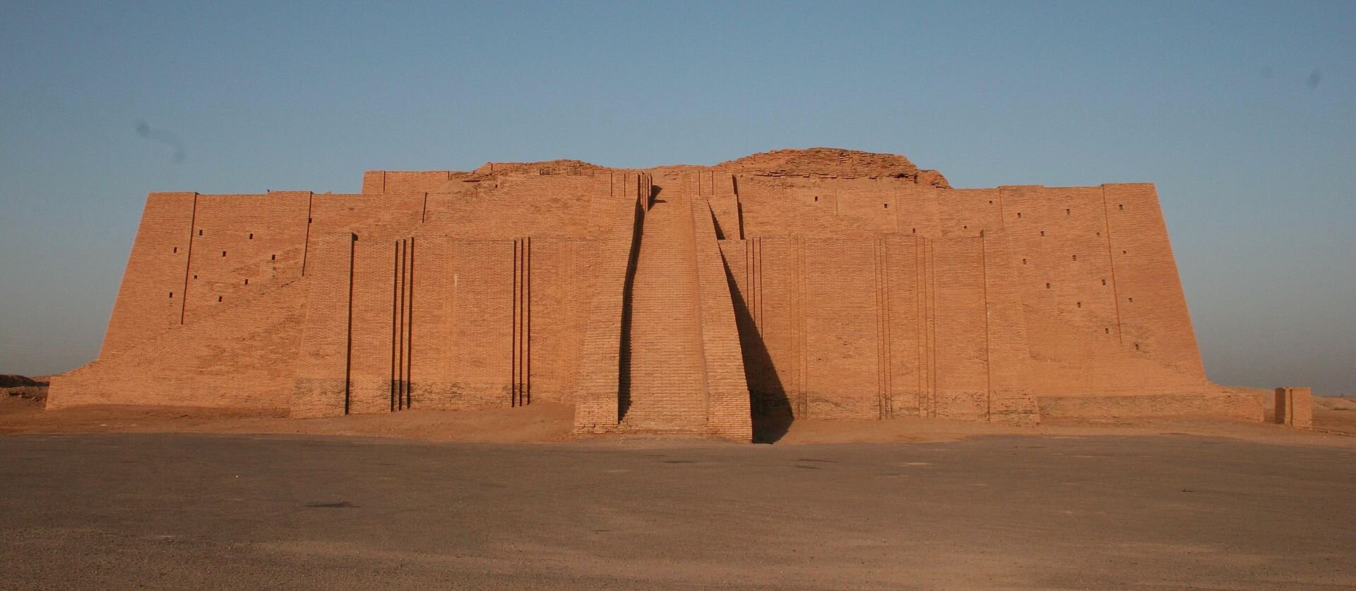 Ilustracja przedstawia zikkurat, monumentalną świątynie z czerwonej cegły o zmniejszających się schodkowo kolejnych tarasach. Na szczyt świątyni prowadzą szerokie schody usytuowane od frontu i po obu stronach.