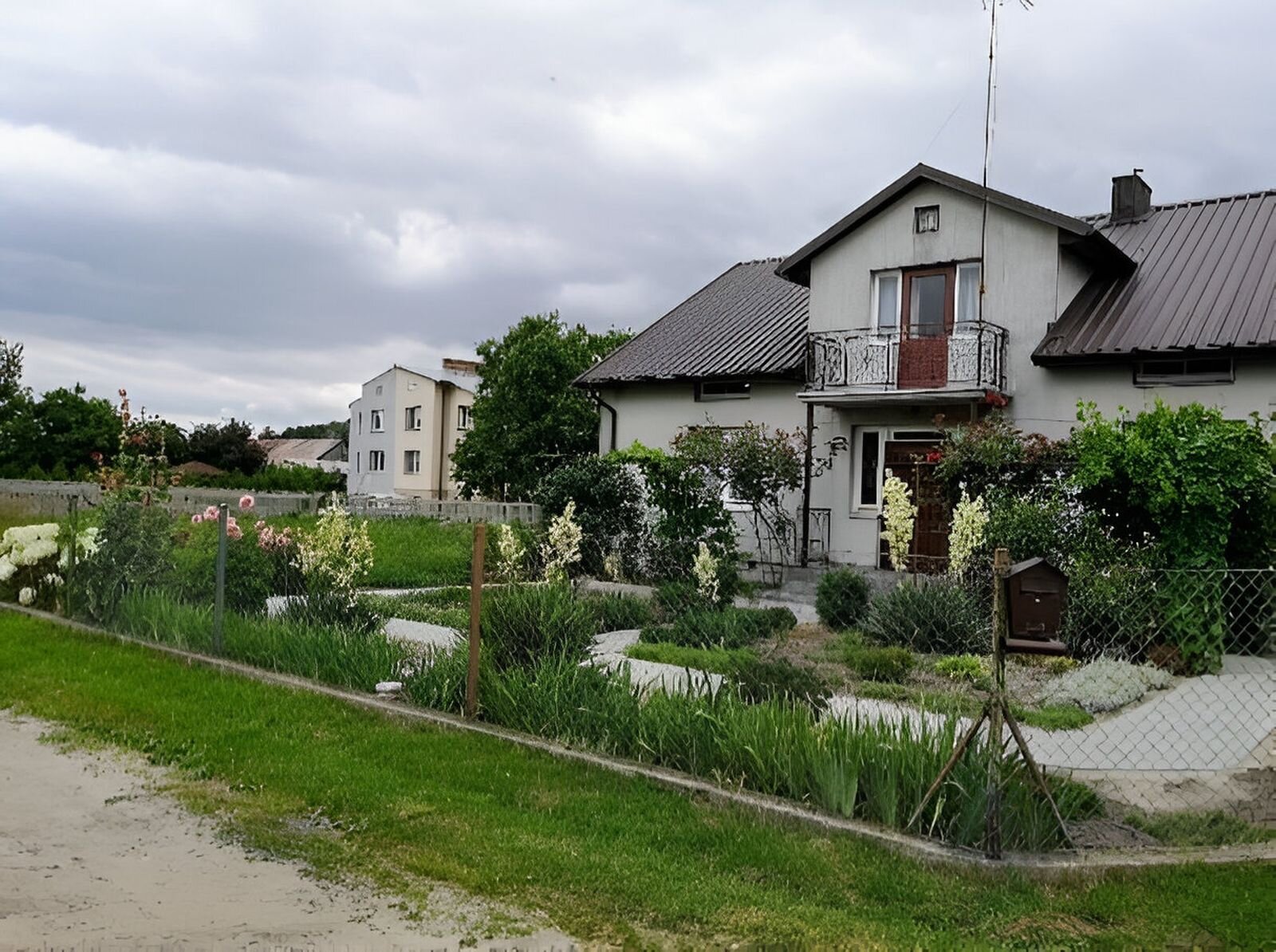 Fotografia przedstawia dwa domy położone w sąsiedztwie. Po prawej dom z szarą elewacją, po lewej piętrowy dom w połowie szary w połowie beżowy. 