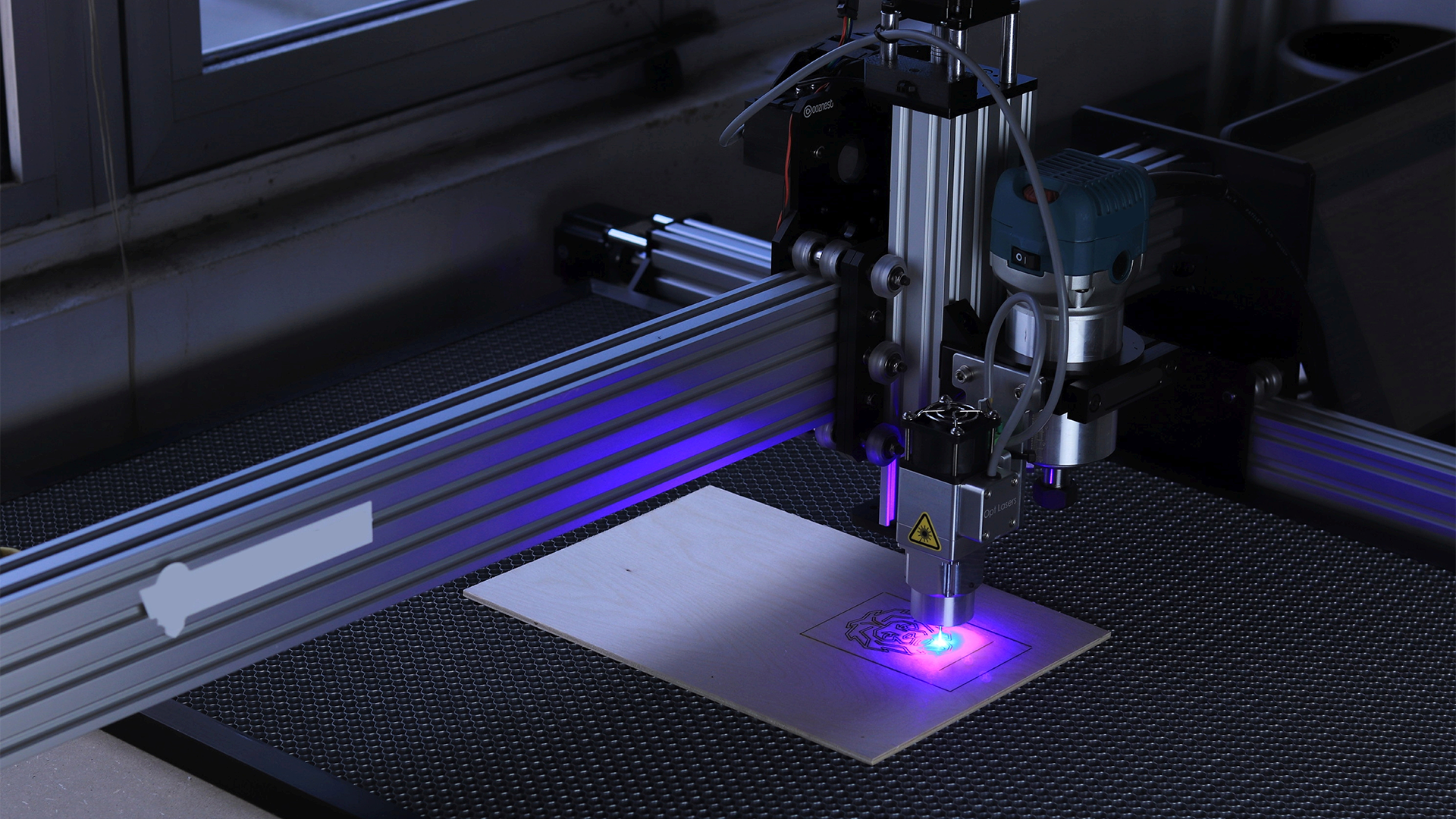 Grafika przedstawia cięcie laserowe. Na płycie stanowiska roboczego znajduje się komponent, na którym za pomocą lasera wycinane są pożądane kształty.