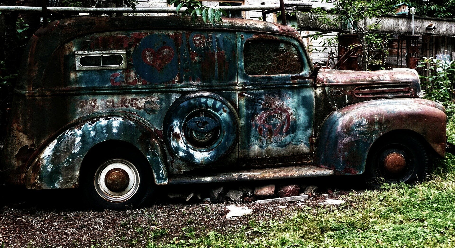 Zdjęcie przedstawia stary, zaniedbany samochód, którego karoseria jest zniszczona. Na powierzchni znajdują się plamy, powierzchnia wydaje się chropowata.