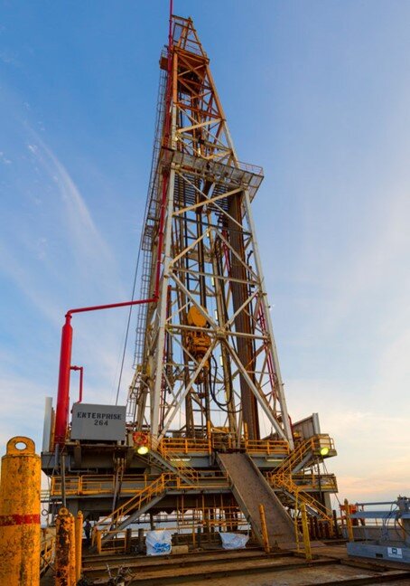 Na zdjęciu widać wieżę wiertniczą. Widoczne wieża jest konstrukcją kratową o kształcie ostrosłupa ściętego. W dolnej części zdjęcia widoczny jest podest w formie podbudowy. Z podestu do poziomu gruntu prowadzi pochylnia. Po lewej stronie podbudówki znajduje się cienki czerwony cylindryczny kształt od którego odchodzi czerwona rura. Rura biegnie do szczytu wieży.  Ze szczytu wieży biegną liny na końcu których zamontowane jest urządzenie o kształcie ósemki.W tle zdjęcia widać wodę.