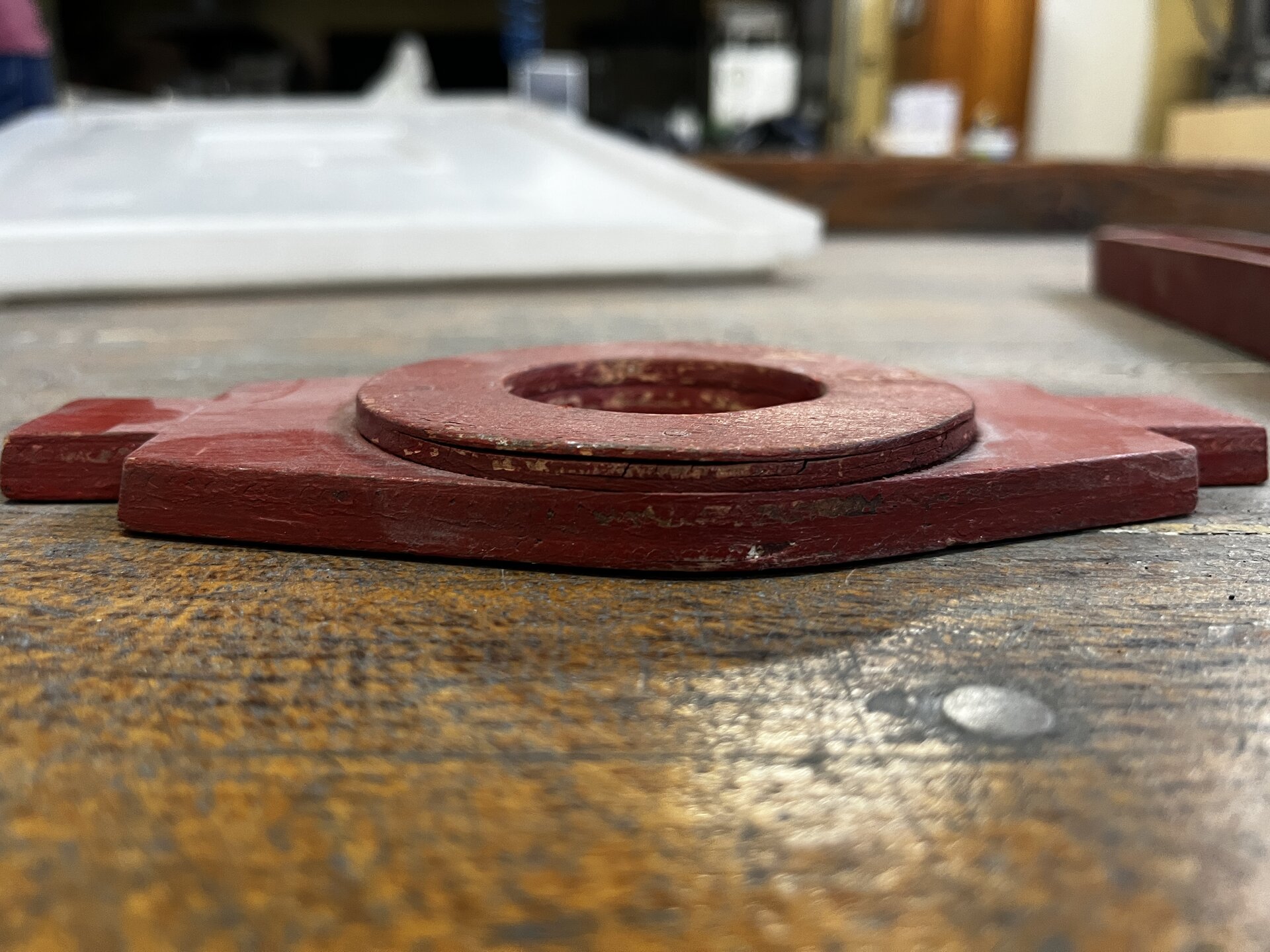 Na zdjęciu pokazano drewniany model odlewniczy z widocznymi rozwarstwieniem drewna. W centralnej części ekranu widoczny jest model zbudowany z połączenia prostopadłościennej podstawy z okręgiem. Widoczny okrąg znajdują się na podstawie ma rozwarstwienia w górnej części. Przy krawędzi widoczne jest pęknięcie biegnące po obwodzie okręgu. 