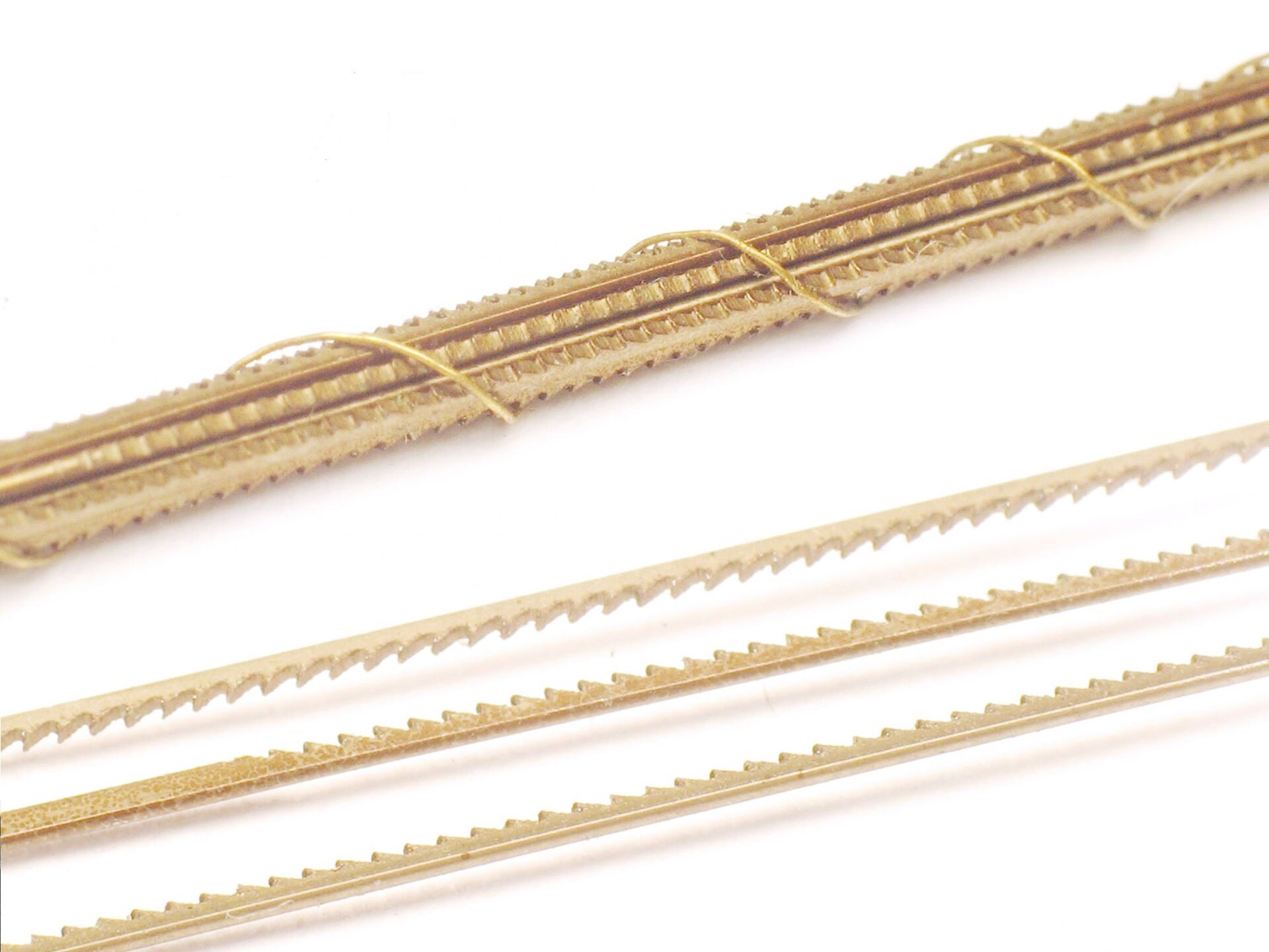 Zdjęcie przedstawia trzy leżące luzem piłki do metalu. Są one wąskie, podłużne, z niewielkimi zębami. W ich pobliżu leży kilka piłek owiniętych cienkim drutem metalowym. 