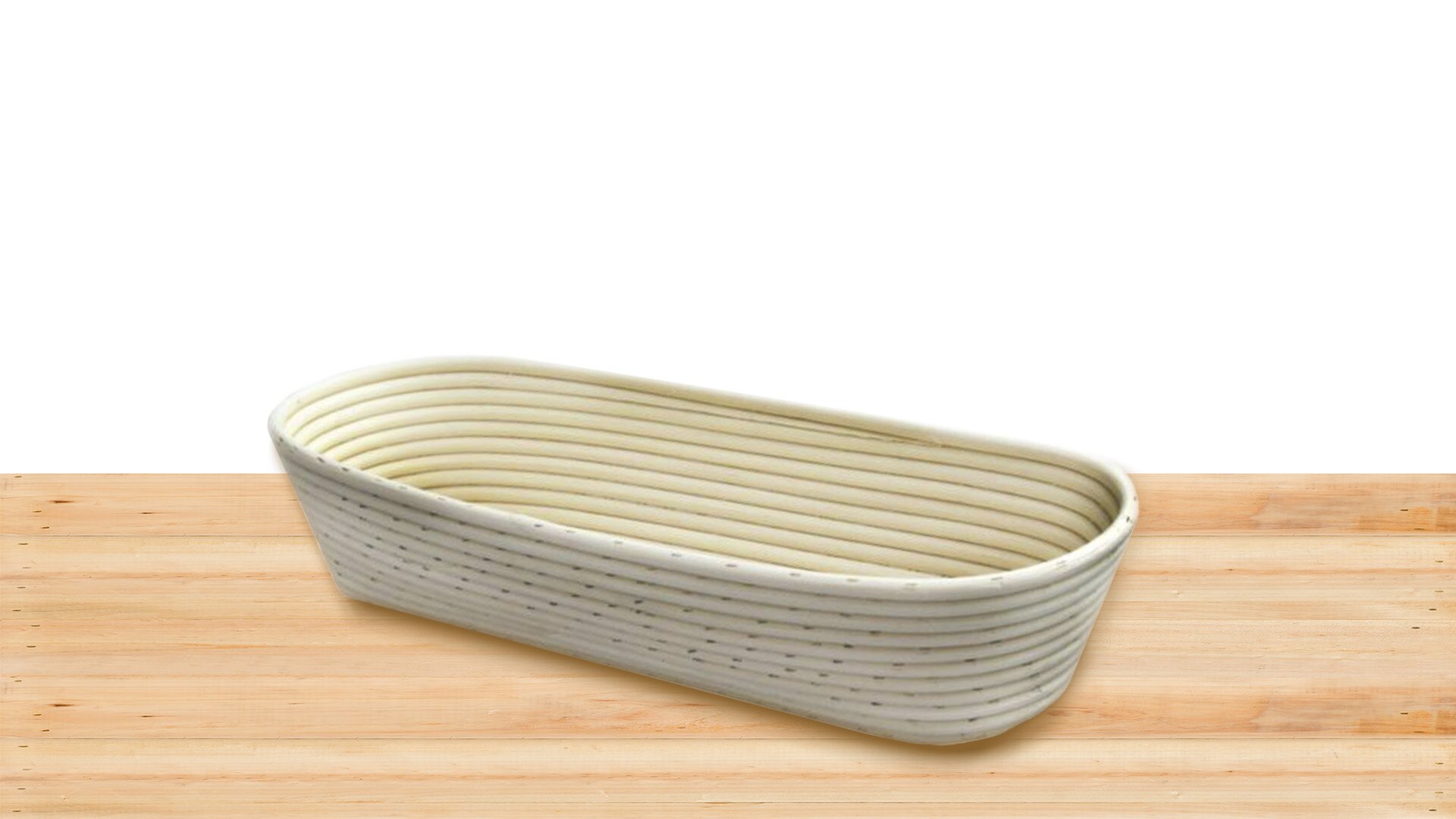 Zdjęcie przedstawia biały wiklinowy koszyk ułożony pod skosem na drewnianym jasnobrązowym blacie. Koszyk ten ma podłużny, owalny kształt oraz jest szerszy w swojej górnej części. Widoczne są na nim poziome, owalne wiklinowe pasy z niewielkimi dziurkami.