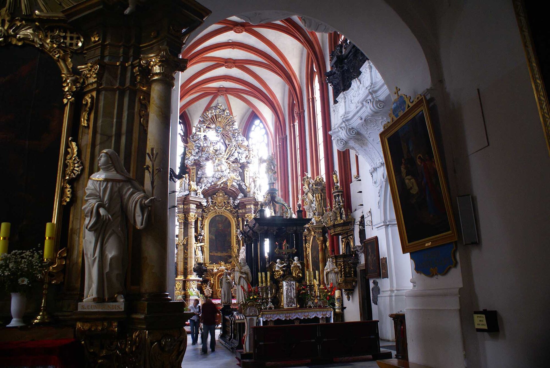 Zdjęcie przedstawia wnętrze kościoła. Widać ołtarz ze złotymi zdobieniami, sklepienie, obrazy na ścianach w złotych ramach. 
