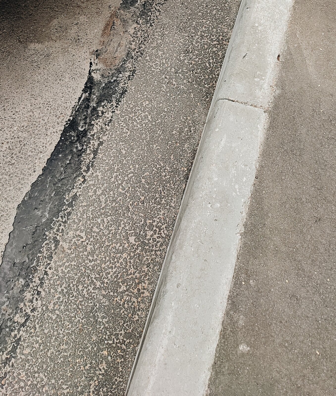 Ilustracja przedstawia fragment szarego krawężnika zamieszczonego przy betonowej drodze.