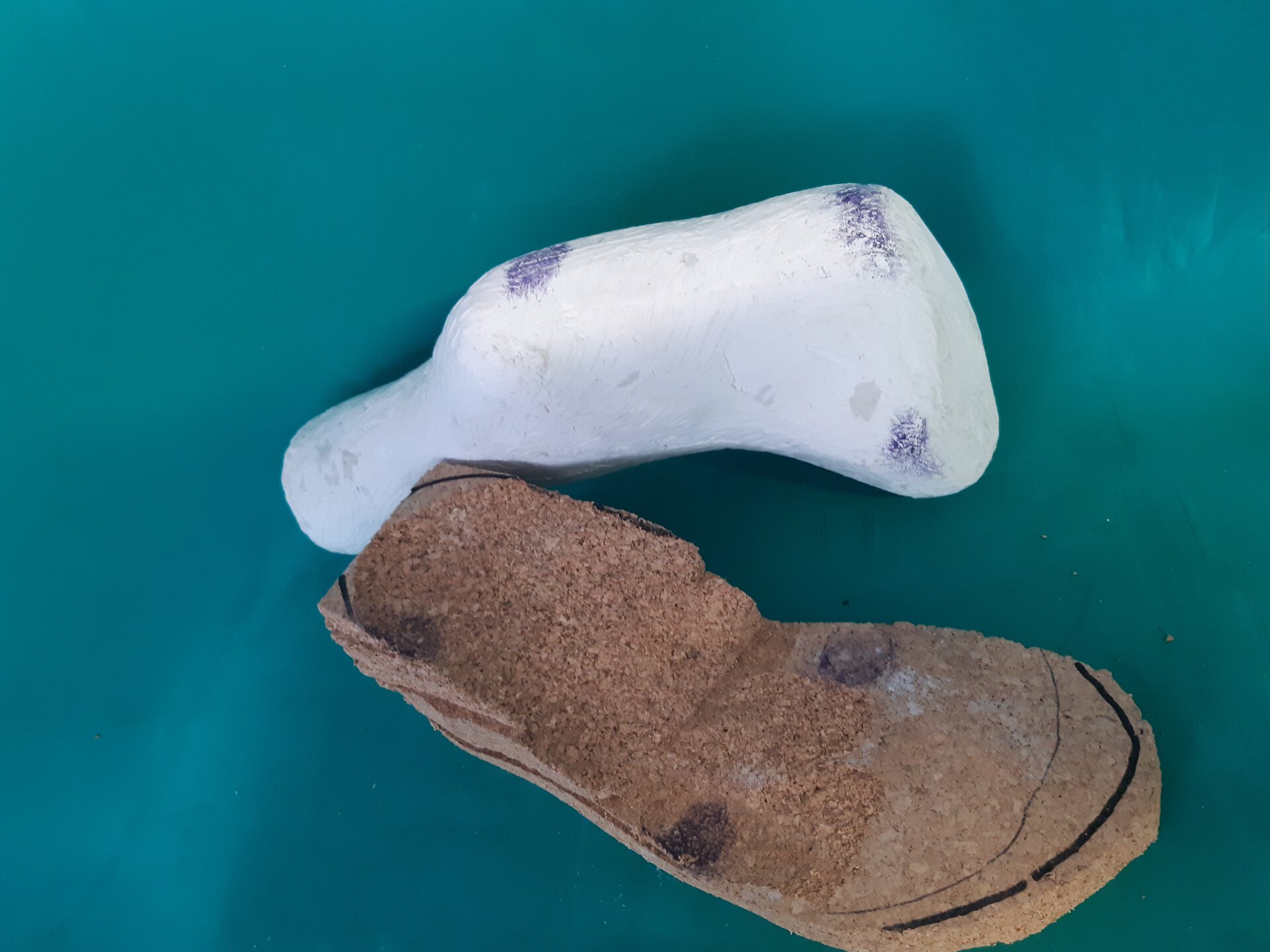 Zdjęcie przedstawia odlew gipsowy stopy oraz wstępny kształt wkładki z płyt suberytowych, z zaznaczonymi bolesnymi miejscami.