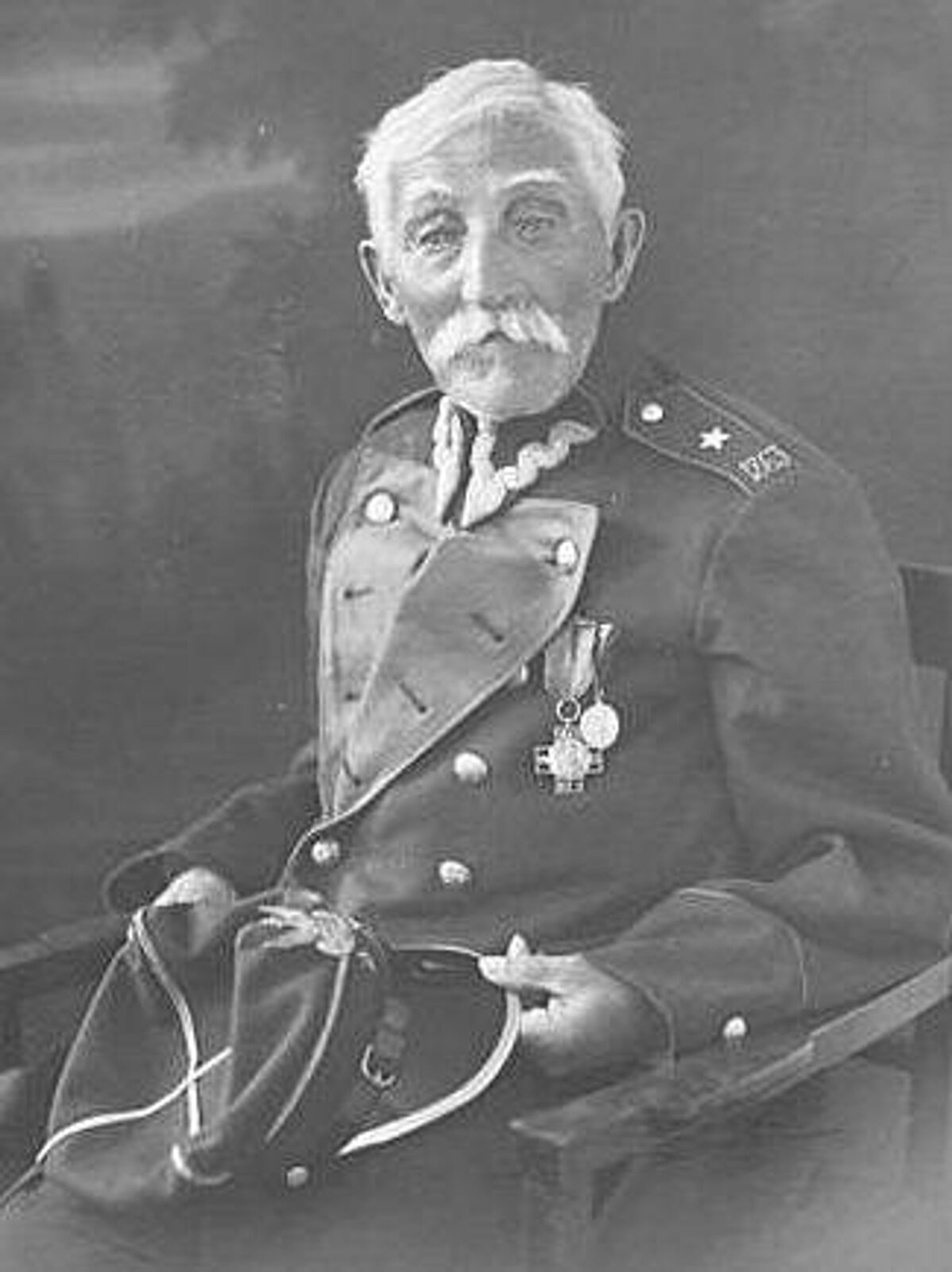 Fotografia przedstawia powstańca styczniowego z siwymi włosami i wąsami w stroju podporucznika. Siedzi na krześle i trzyma na kolanach rogatywkę. Na piersiach po lewej stronie ma przypięte dwa przyznane mu odznaczenia za waleczność.